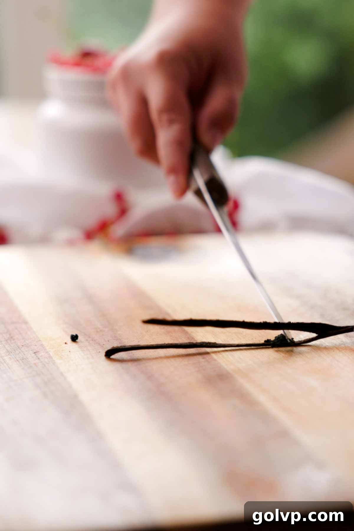 A knife scraping out vanilla bean seeds from a halved vanilla bean.