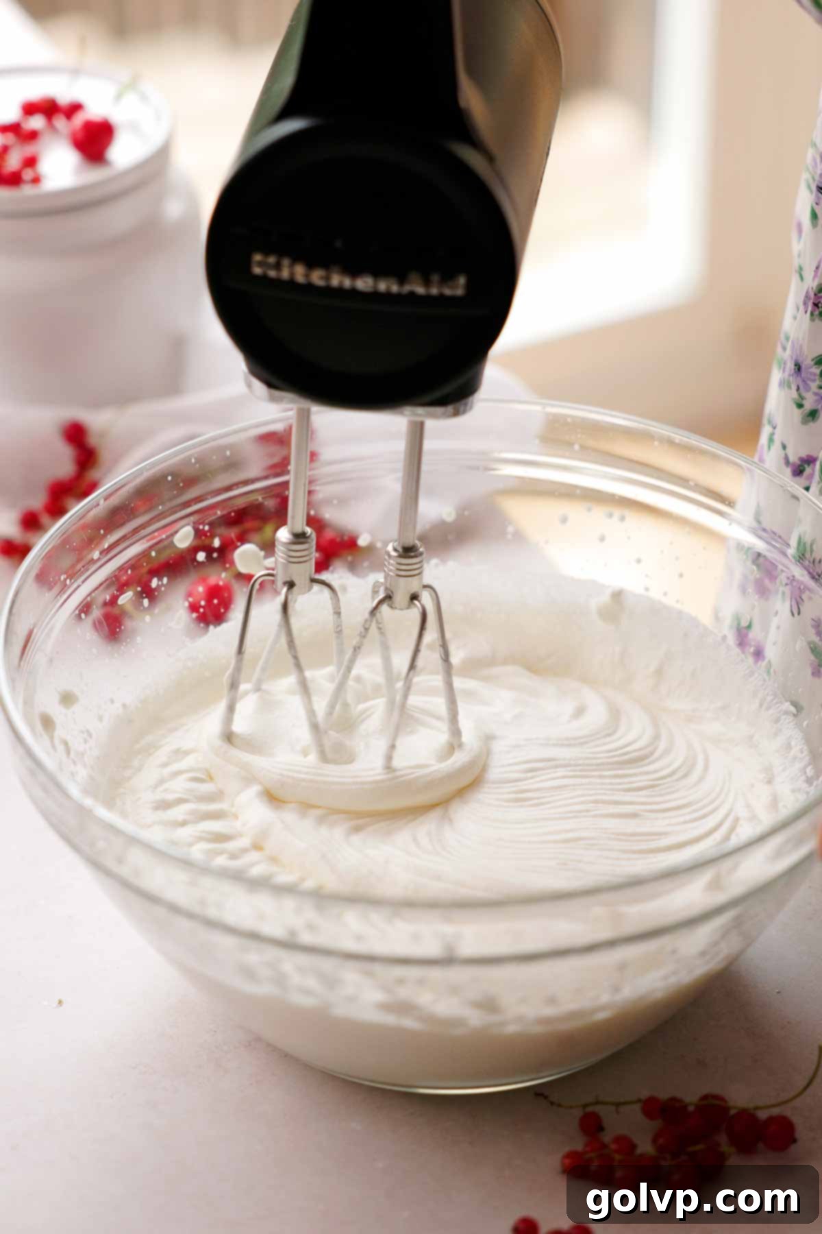 Electric mixer whipping heavy cream in a chilled glass bowl until stiff peaks form.