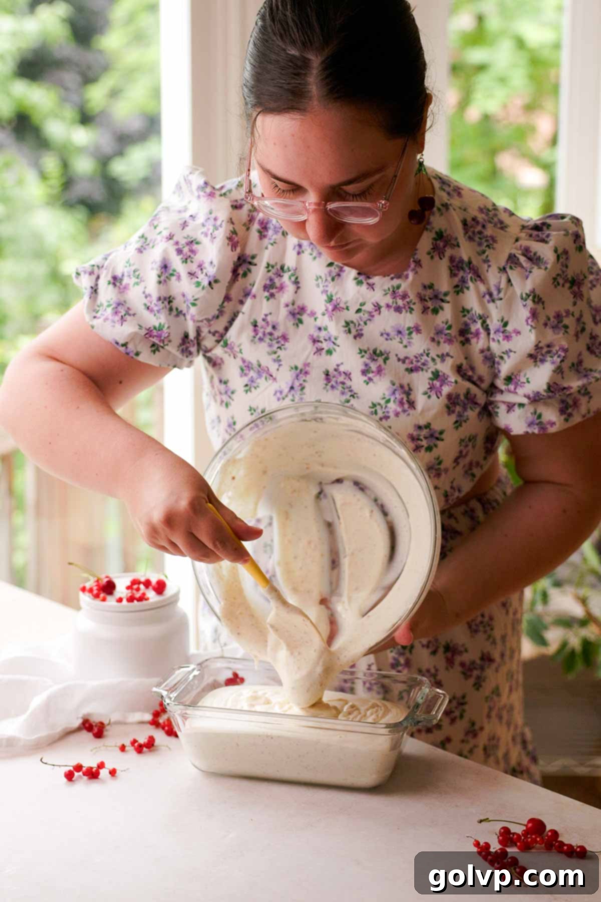 Transferring the vanilla bean brown butter ice cream mixture from a bowl into a glass loaf pan with a spatula.