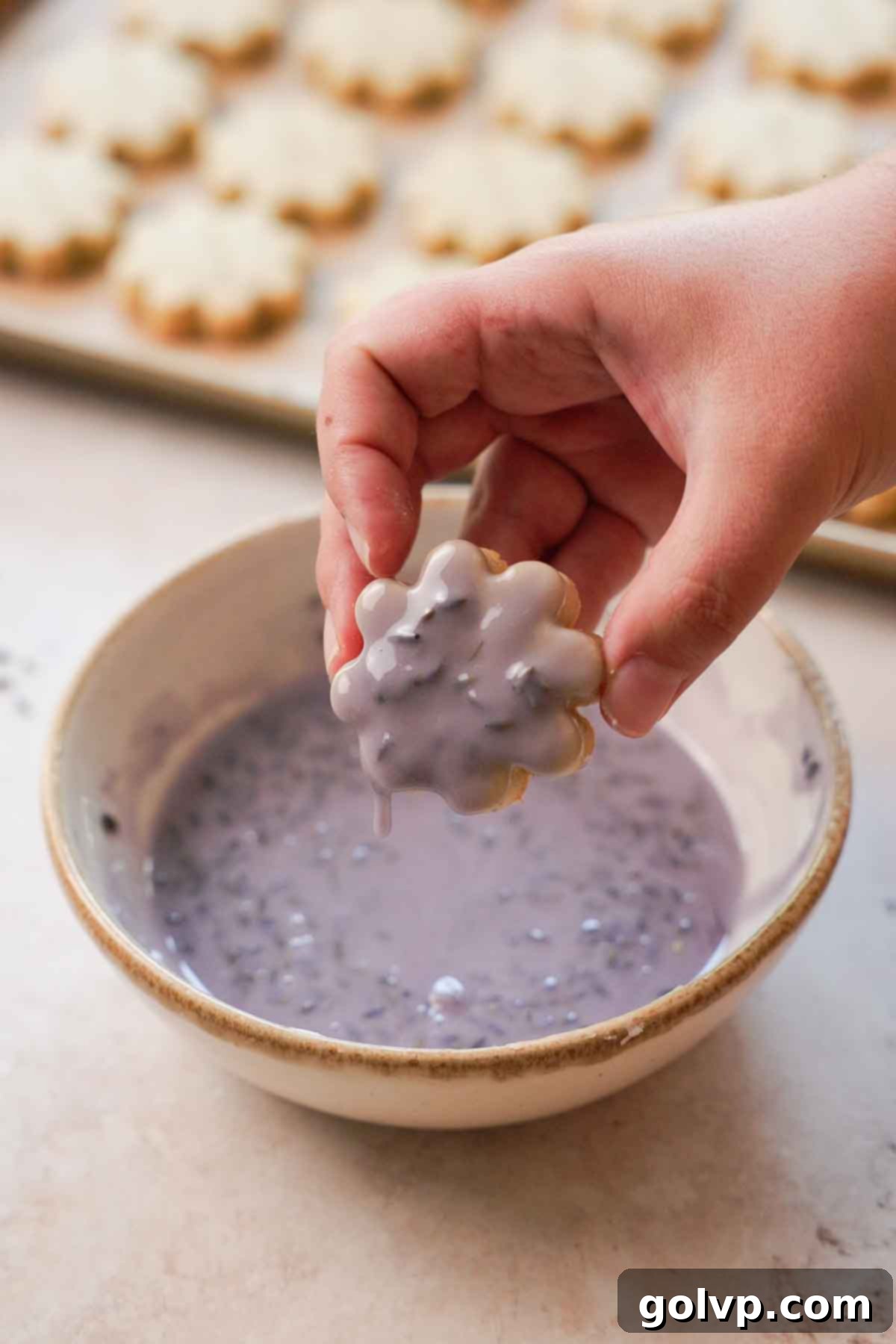 dipping flower shaped cookie into purple lemon lavender glaze