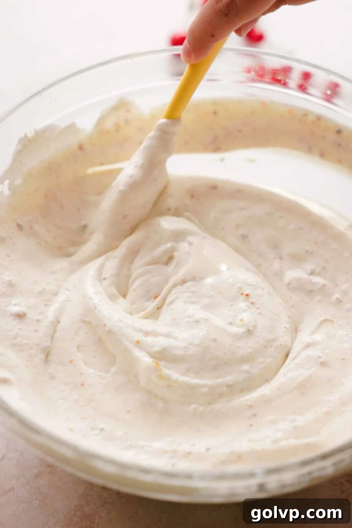 folding whipped cream, condensed milk, vanilla seeds, and brown butter with a spatula in a bowl