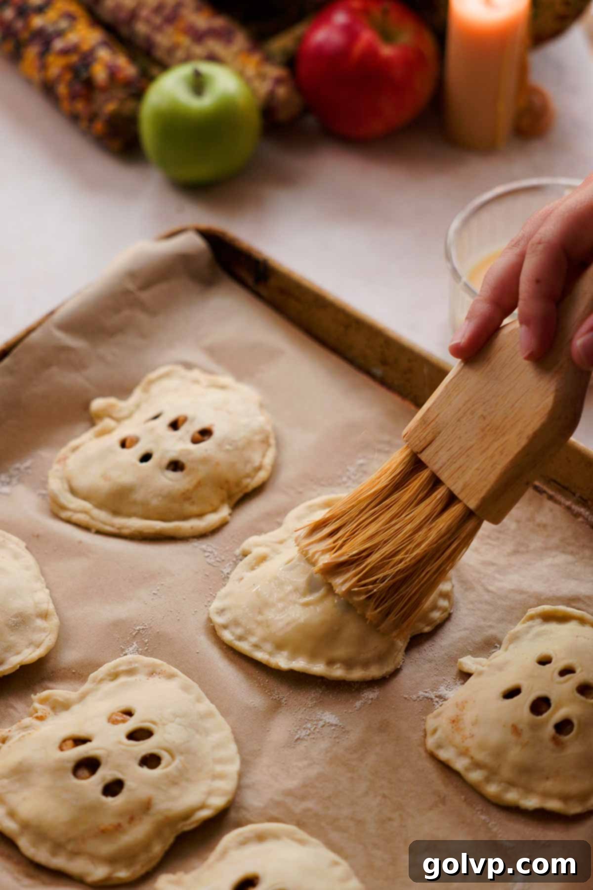 Brushing eggwash over apple-shaped apple hand pies before baking