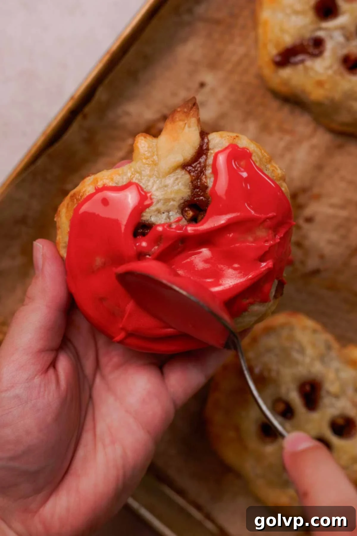 Coating an apple hand pie with glaze using a spoon, creating a beautiful finish