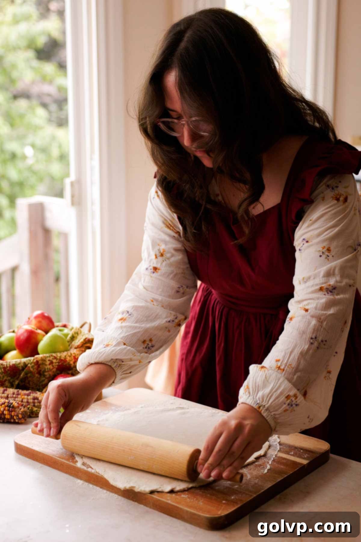 Rolling out a piece of butter pie crust on a floured surface with a rolling pin