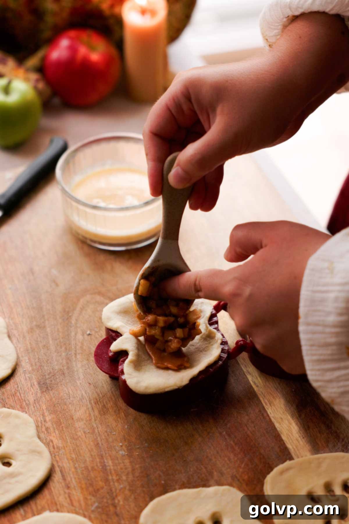 Spooning spiced apple pie filling over a soft caramel placed on an apple-shaped pie crust