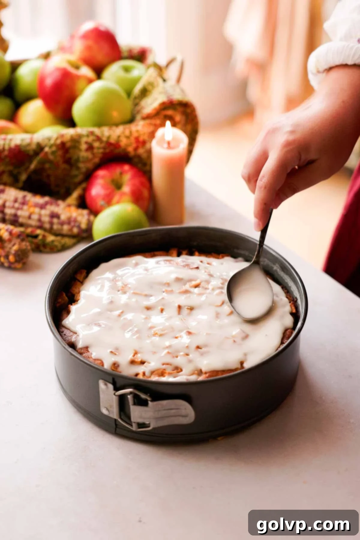 spreading vanilla glaze over apple fritter cake with the back of a spoon