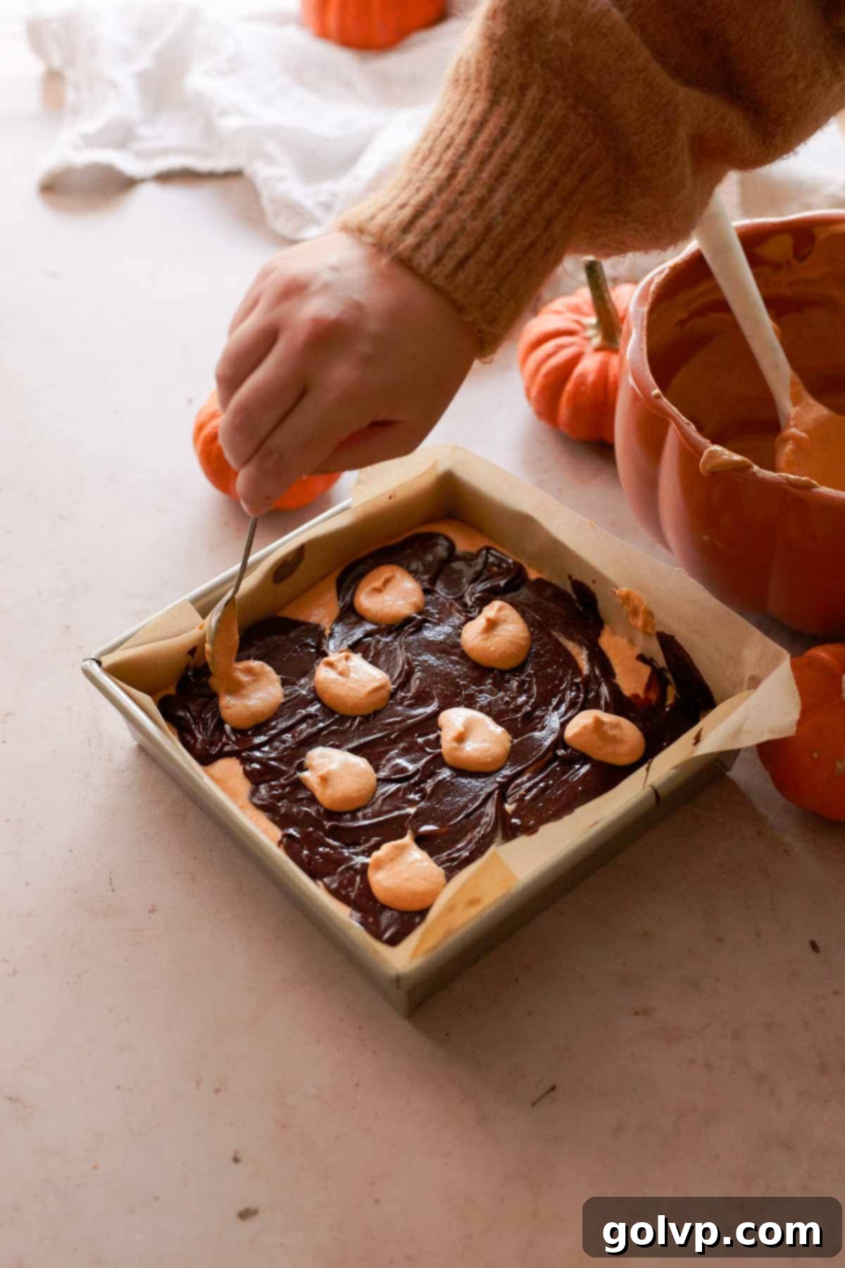 spooning orange cheesecake batter over brownie batter
