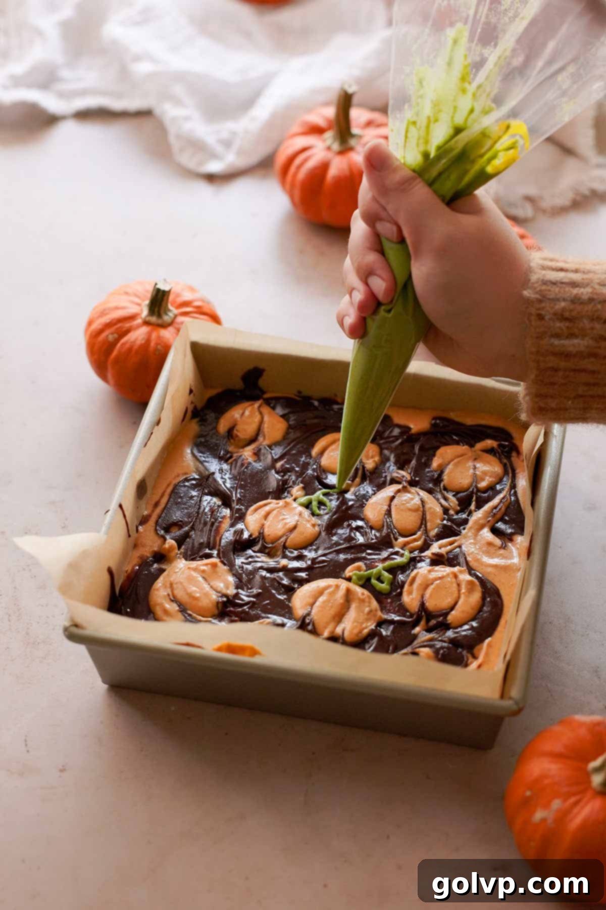 piping green vines onto pumpkin cheesecake swirl brownies with a piping bag
