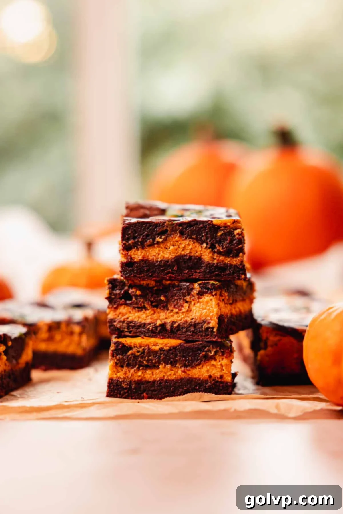 three pumpkin cheesecake layered brownies stacked on top of eachother