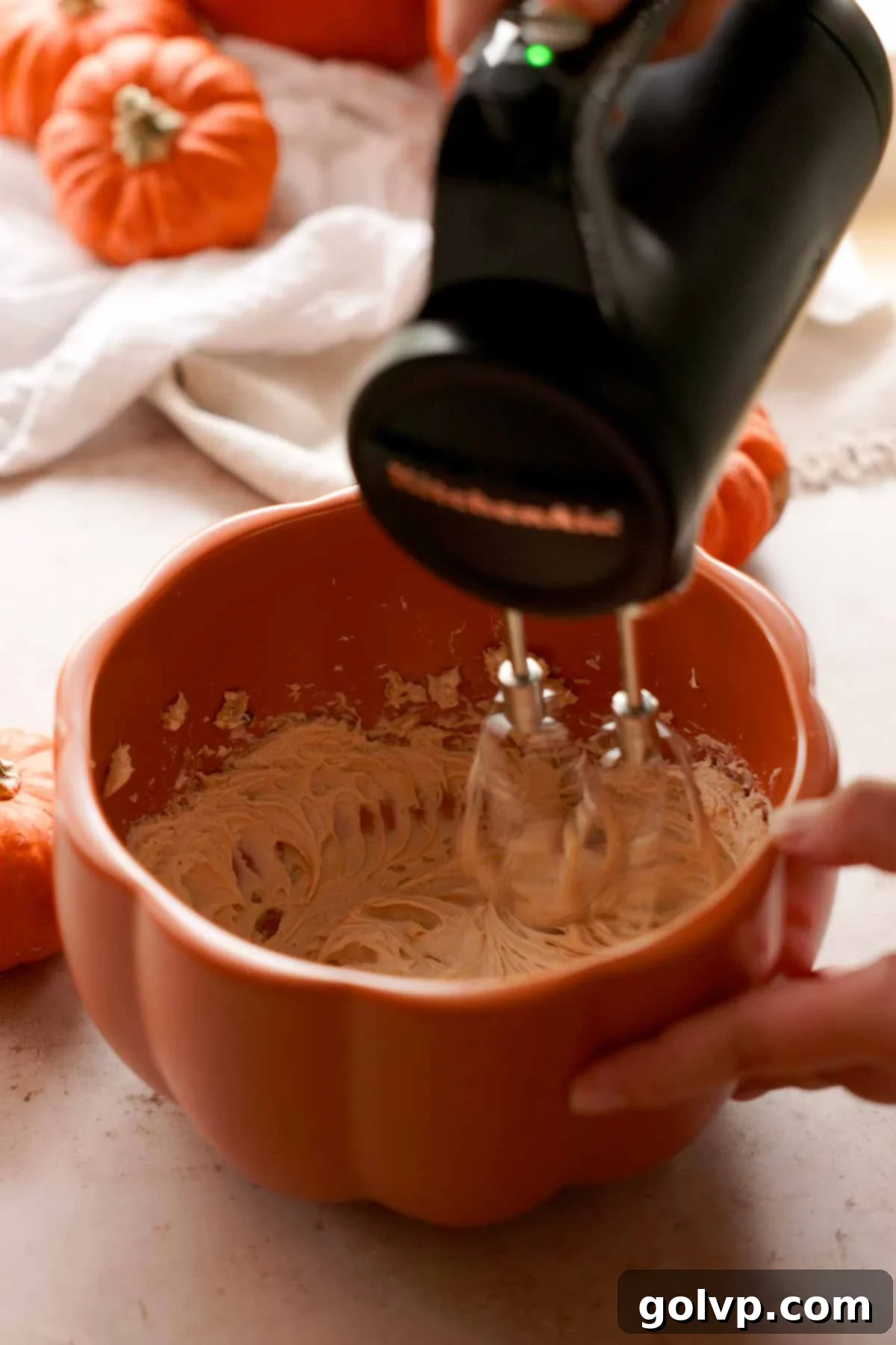 beating cream cheese and brown sugar in a pumpkin shaped bowl with electric mixer