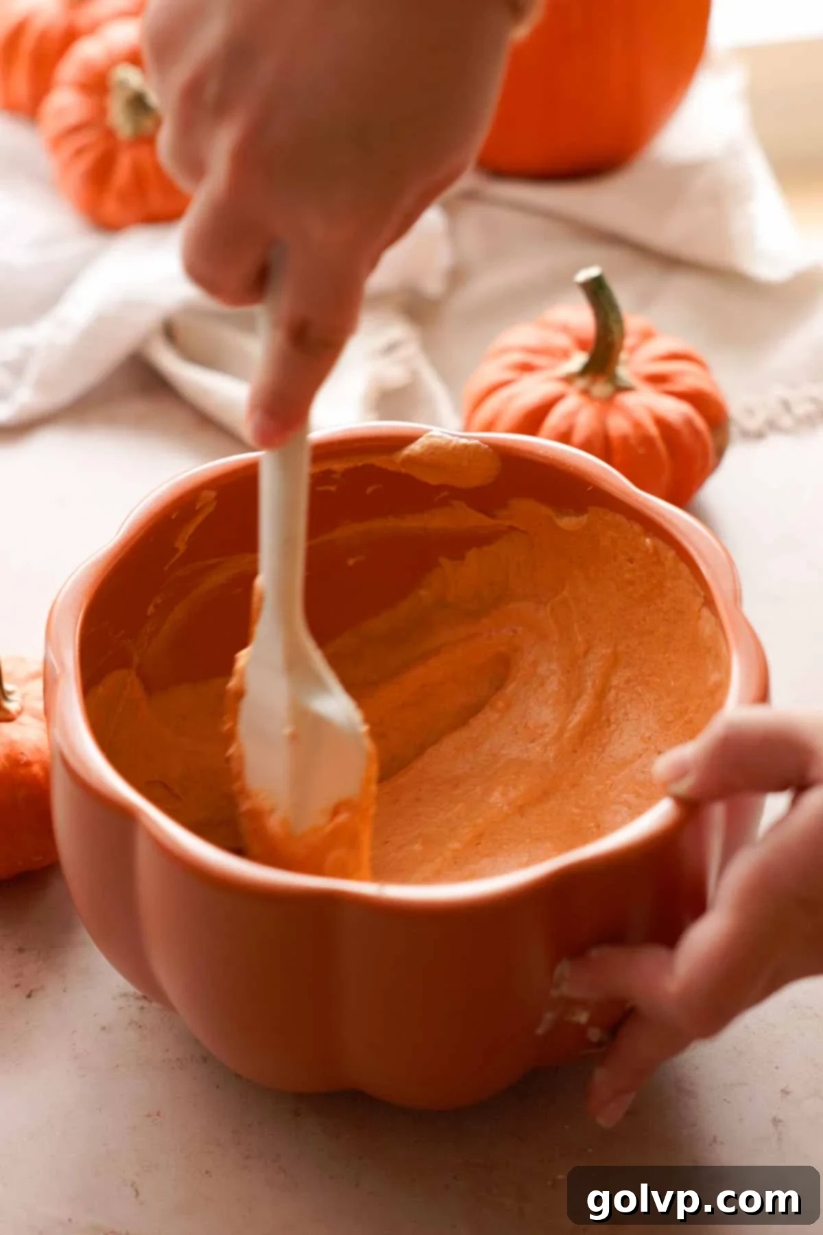 scraping down the edges of the bowl of pumpkin cheesecake batter