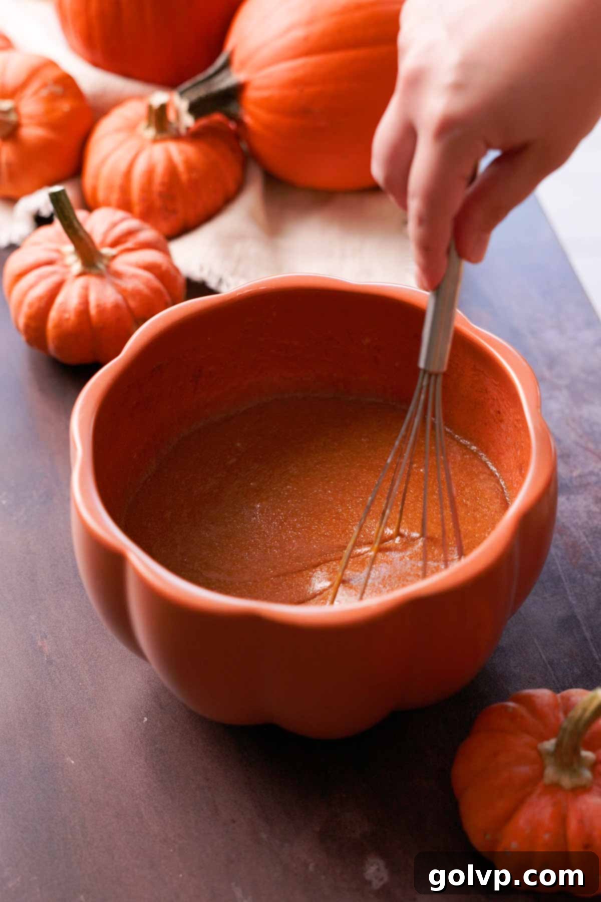whisking pumpkin batter wet ingredients in large pumpkin shaped bowl to combine thoroughly