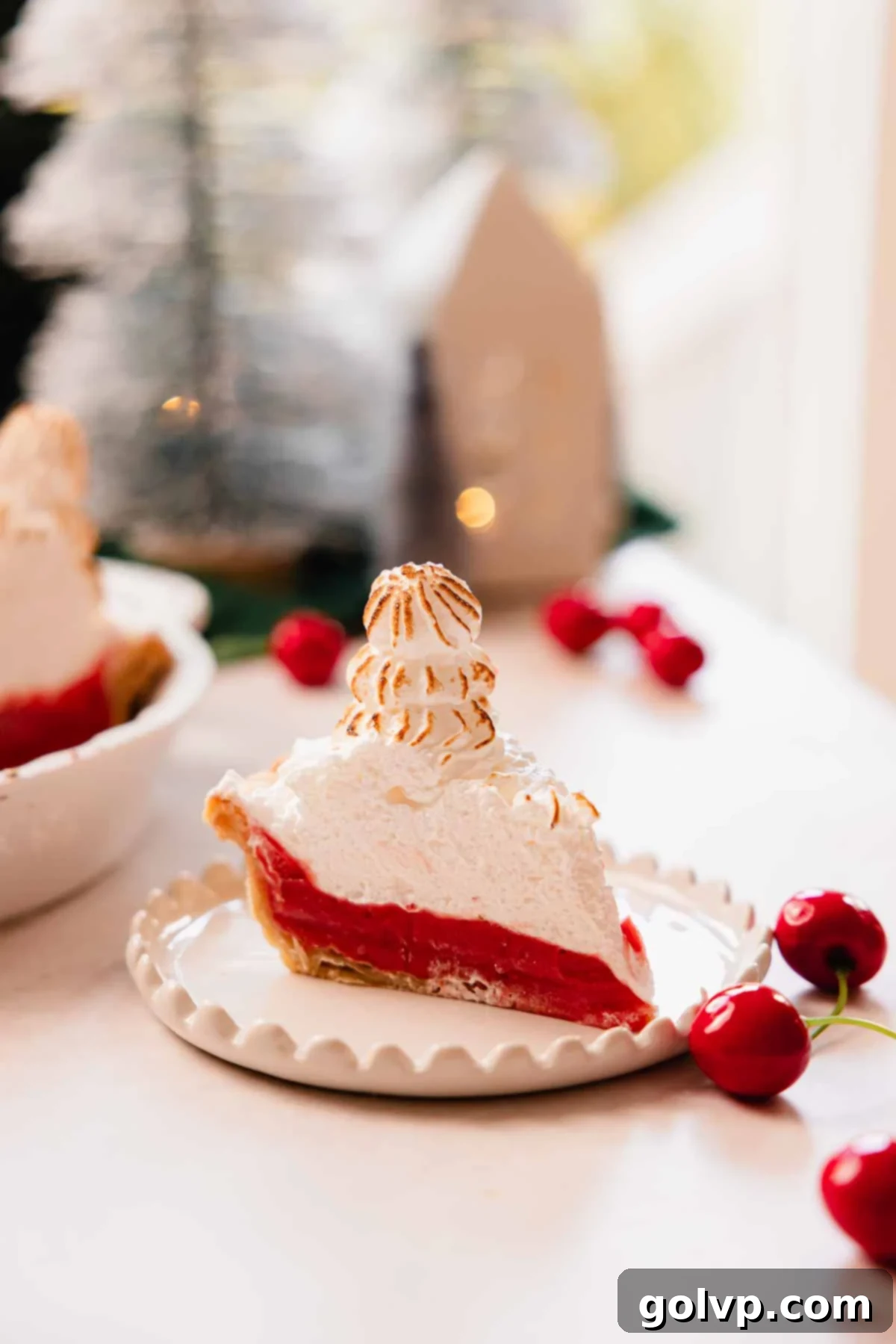 slice of cherry meringue pie on scalloped plate with a tree piped on top