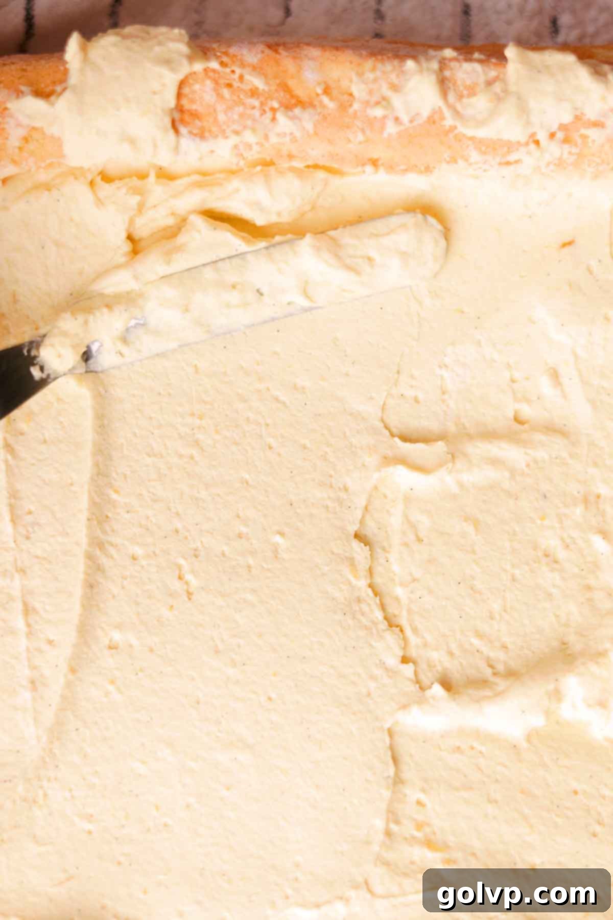 Spreading a generous layer of mango mascarpone filling evenly inside the unrolled sponge cake.