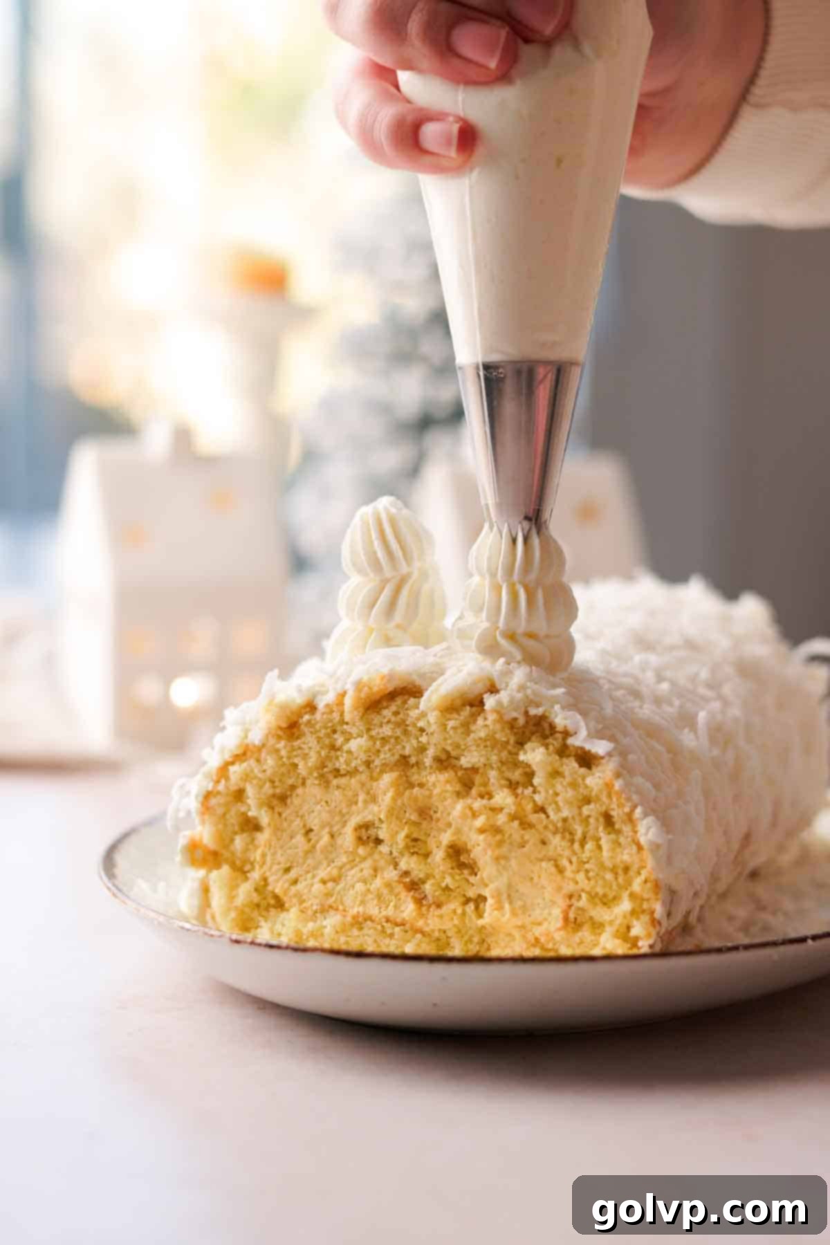 Decorating the mango coconut yule log cake with piped Christmas trees and a star using frosting.