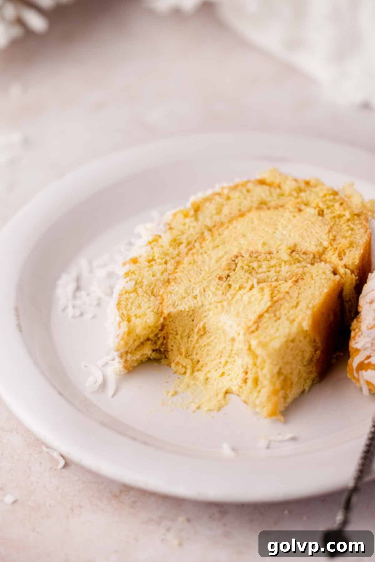 A delectable slice of mango Swiss roll cake on a plate, with a bite taken out to reveal the creamy mango filling and perfect swirl.