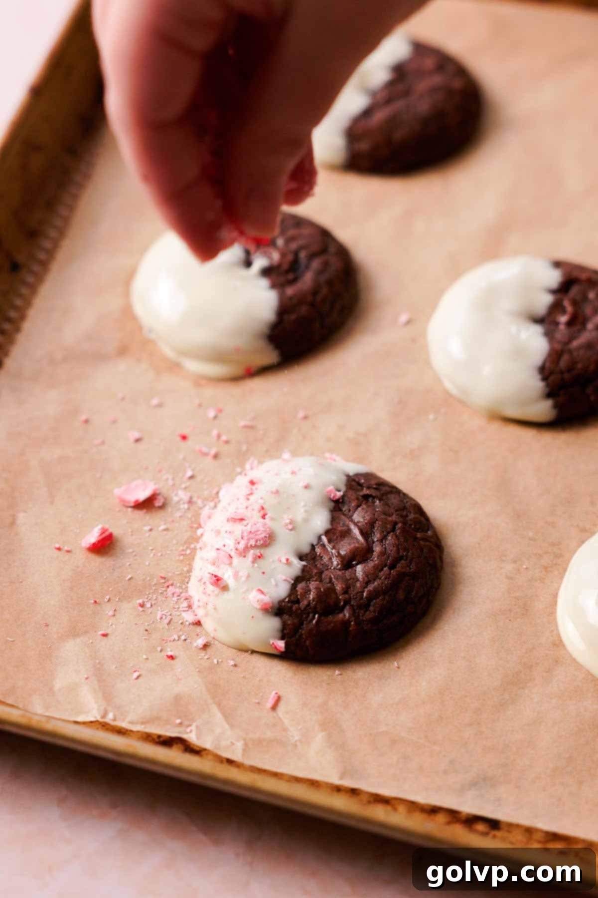 sprinkling crushed peppermint candy canes onto white chocolate dipped cookies