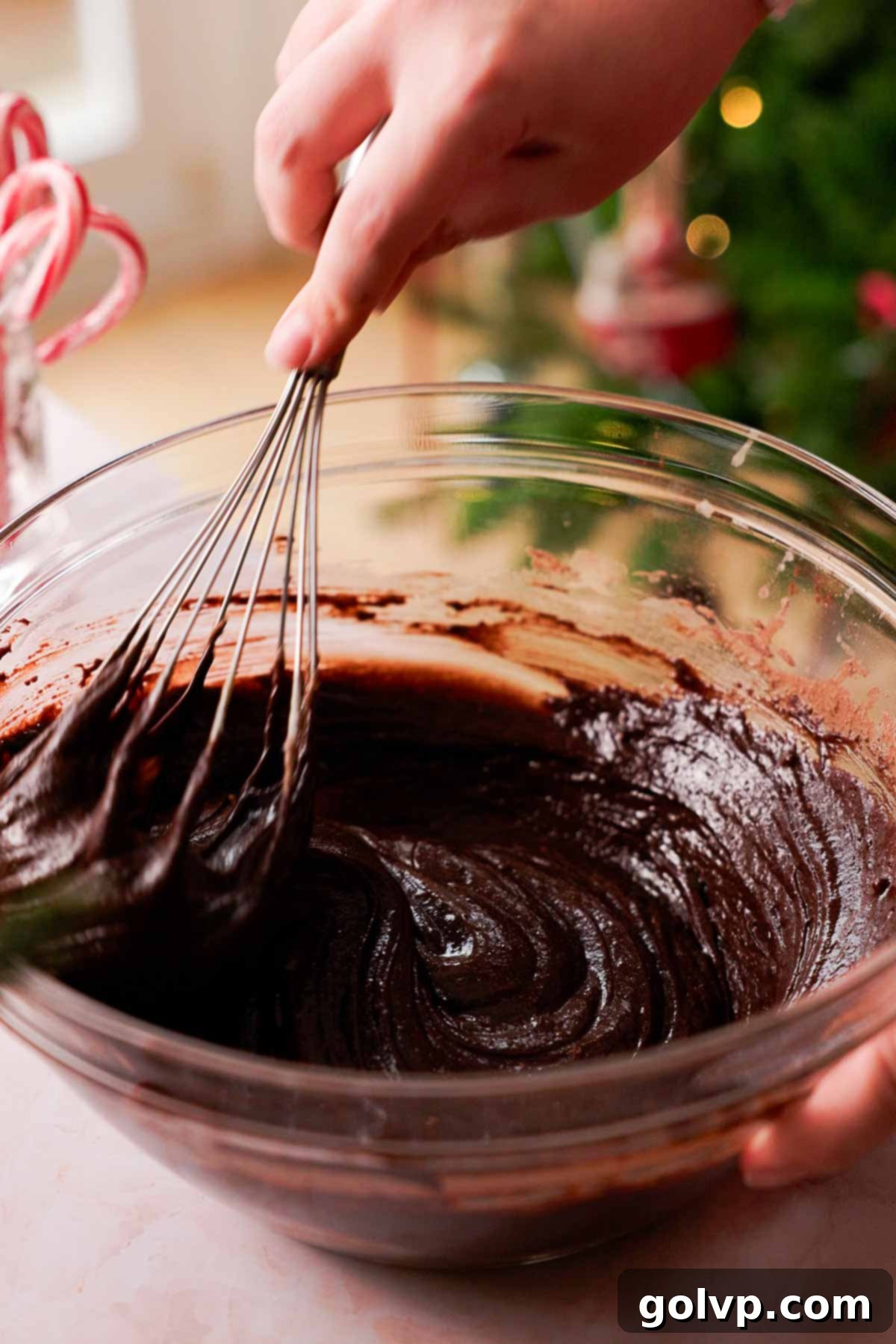 folding brownie cookie dough with a wire whisk in a large glass bowl, incorporating dry ingredients