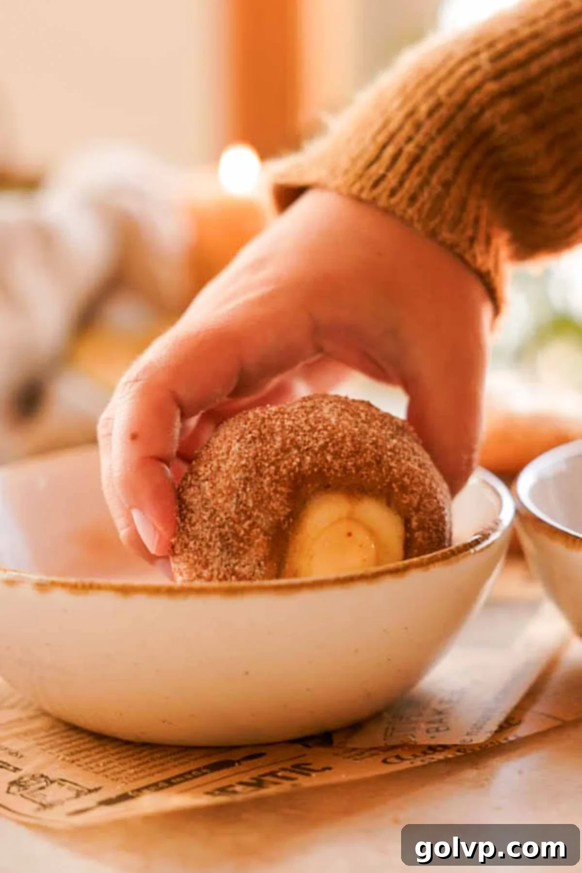 Rolling the brushed apple cider muffin top into cinnamon sugar