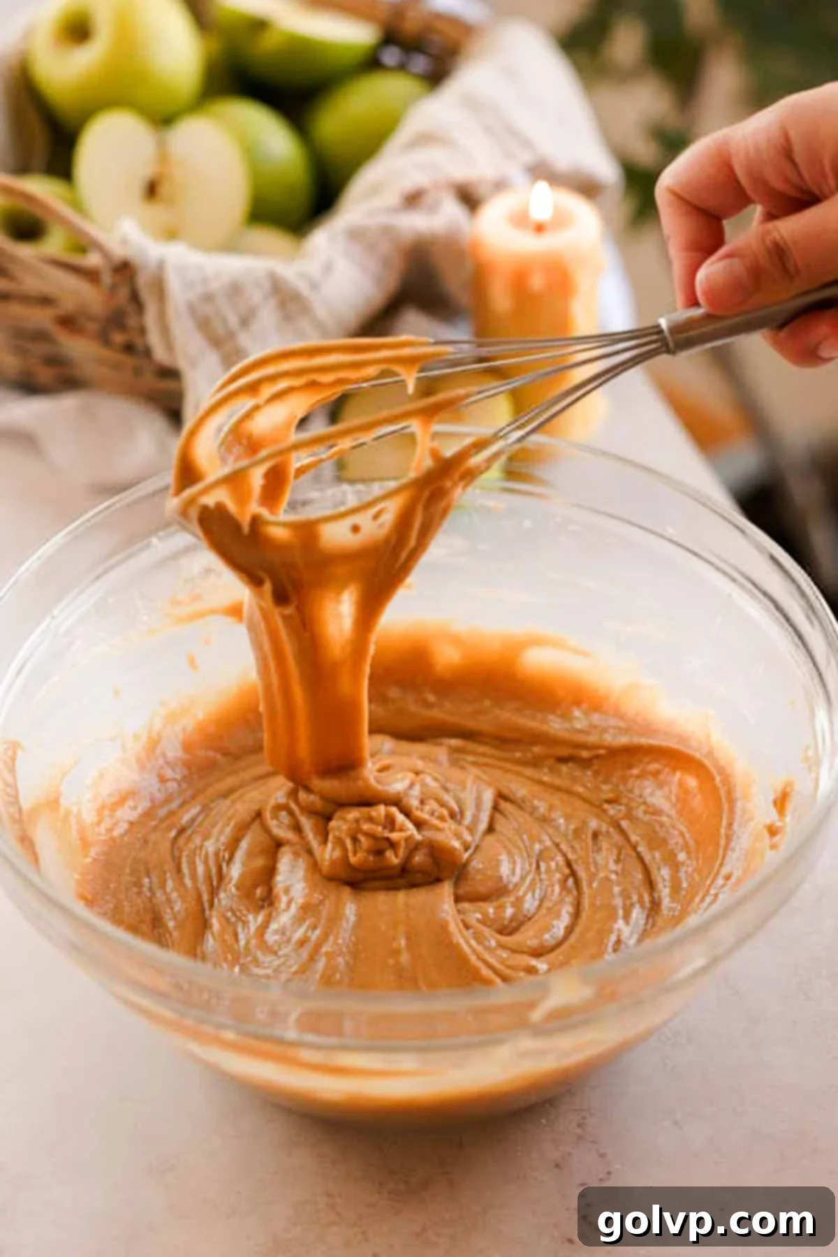 Muffin batter falling off the whisk into a large glass bowl, showing smooth consistency