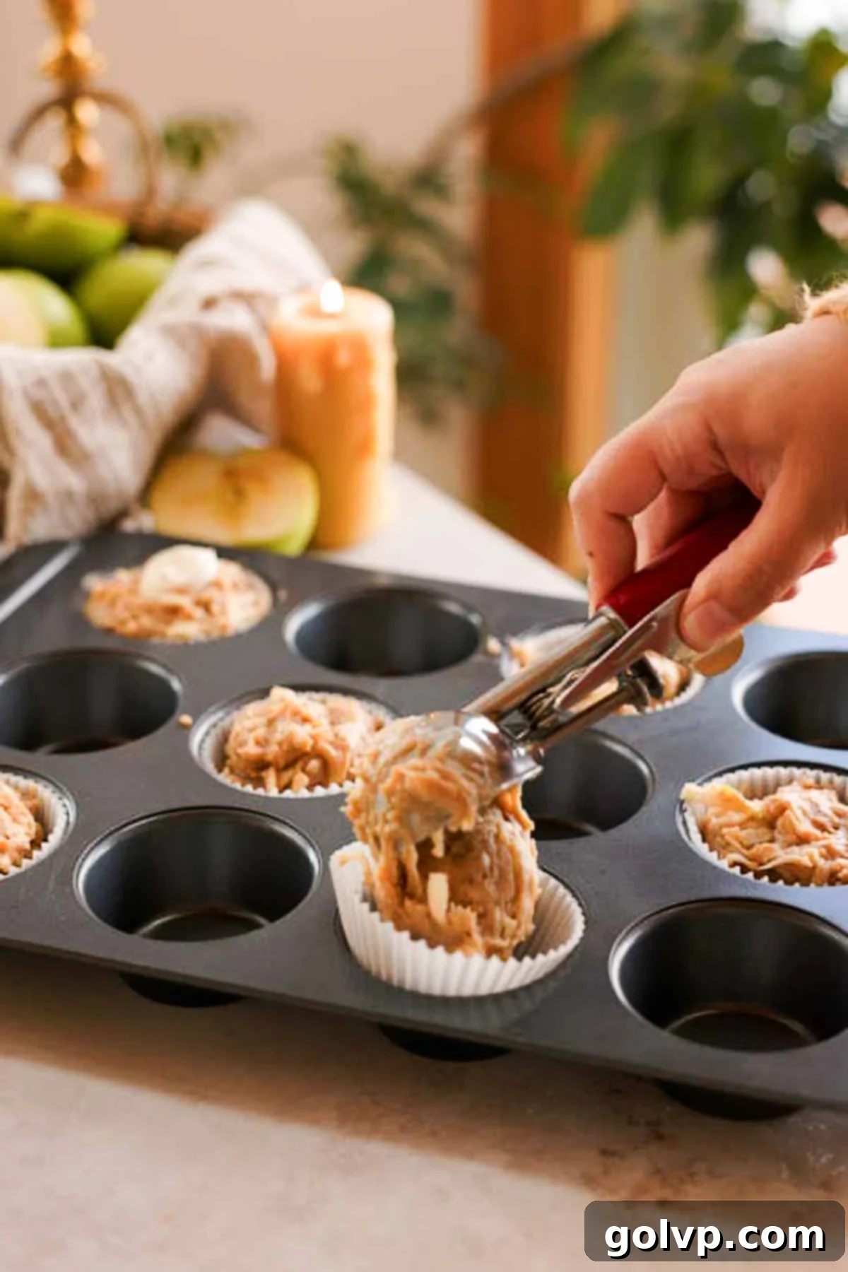 Scooping apple cider muffin batter into muffin liners, filling them generously