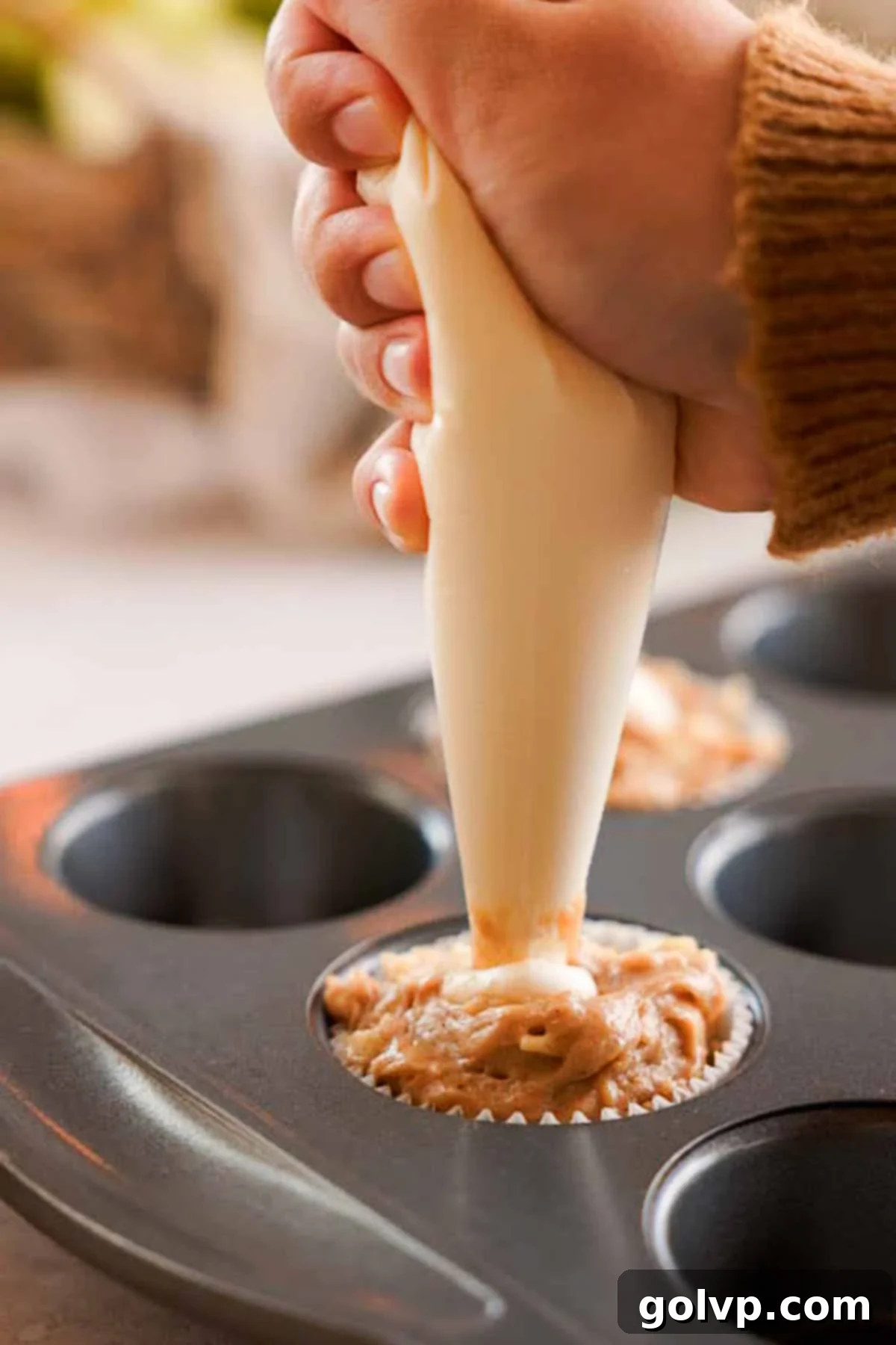 Piping cream cheese filling into the center of muffin batter in a liner