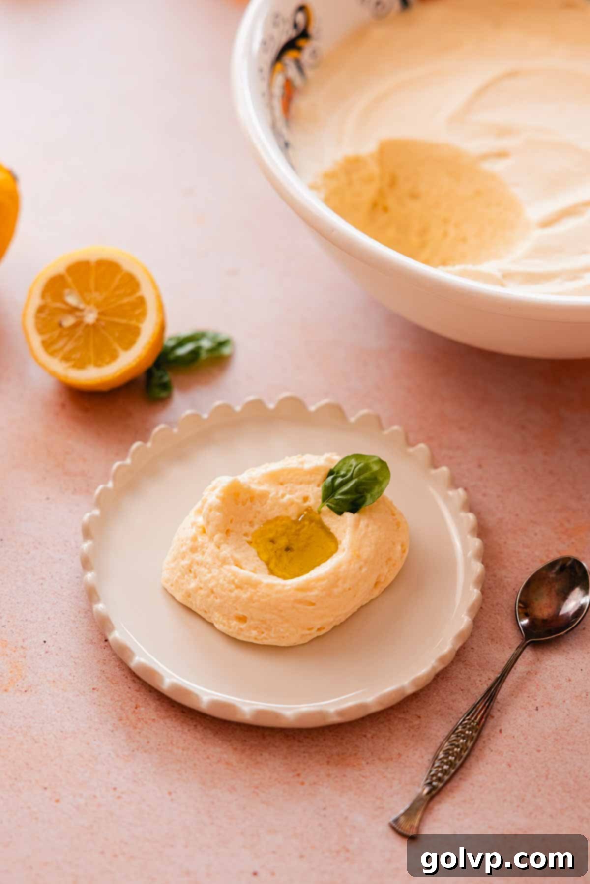 A generous scoop of fluffy lemon mousse, garnished with a drizzle of olive oil and a fresh basil leaf, with a bright lemon curd swirl visible.
