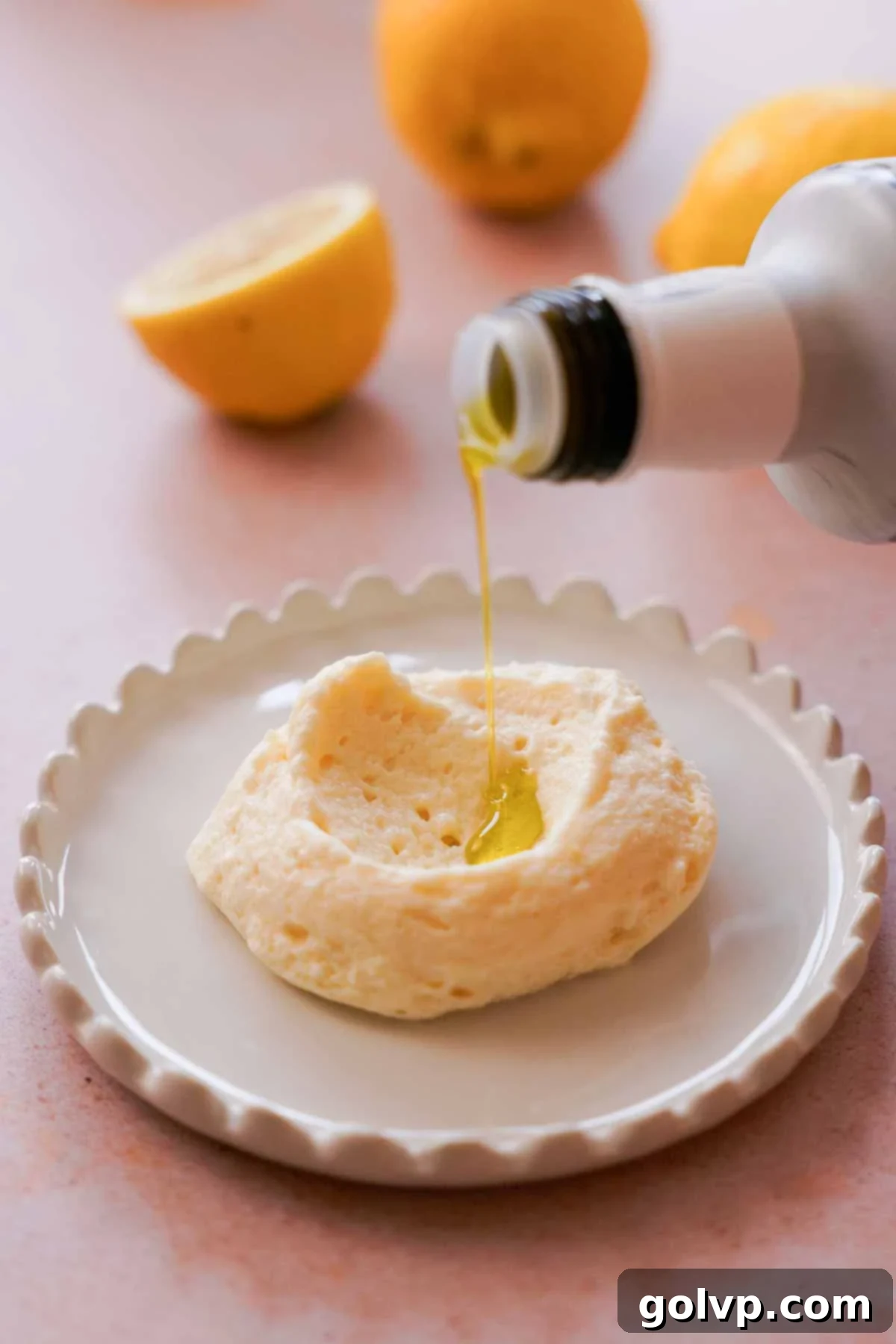A hand drizzling high-quality extra virgin olive oil over a scoop of lemon mousse on a plate.