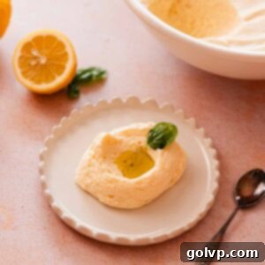 A beautifully presented scoop of fluffy lemon mousse, accompanied by fresh lemon curd, a drizzle of olive oil, and a vibrant basil leaf.