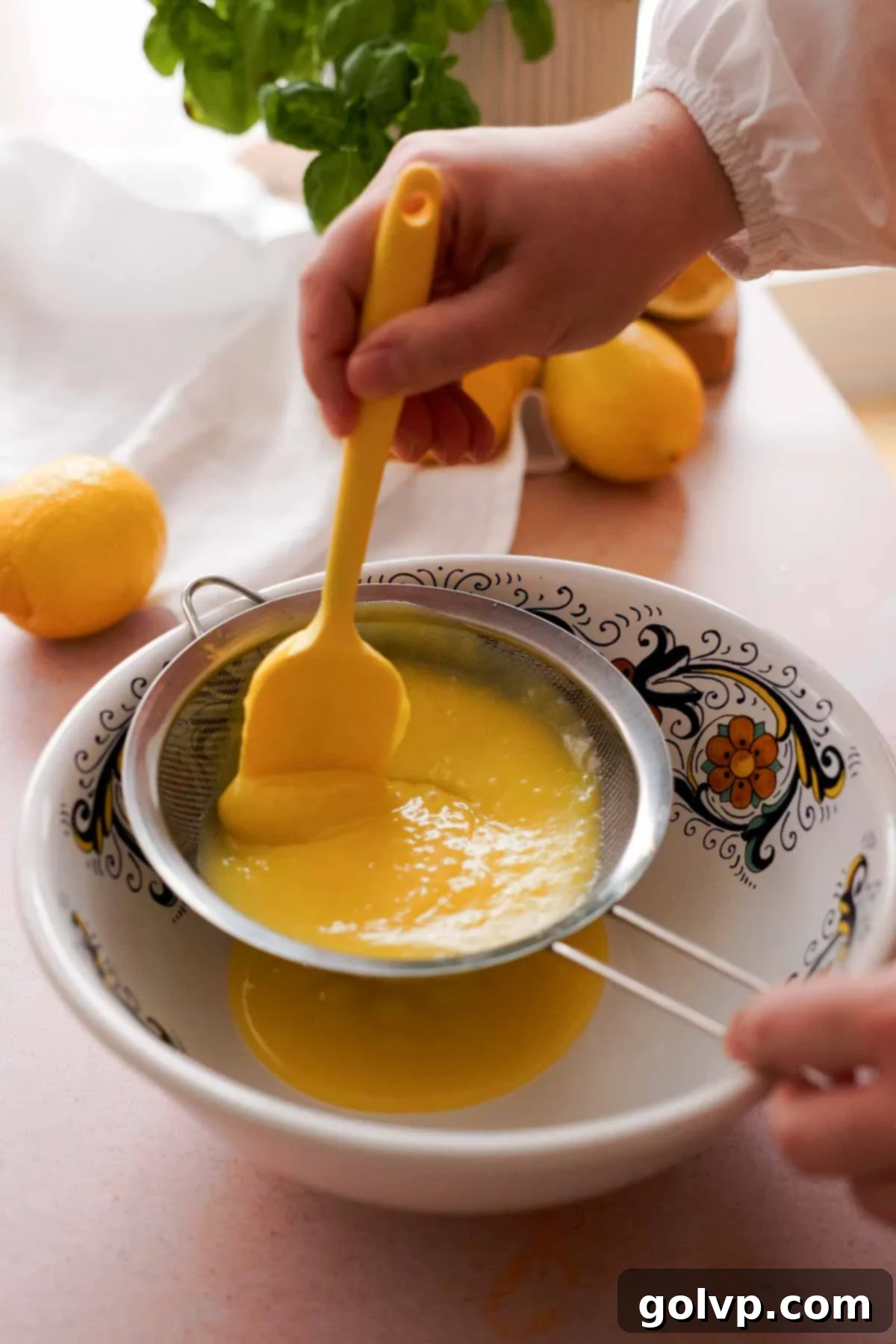 Straining freshly cooked lemon curd through a fine-mesh sieve into a large ceramic mixing bowl.