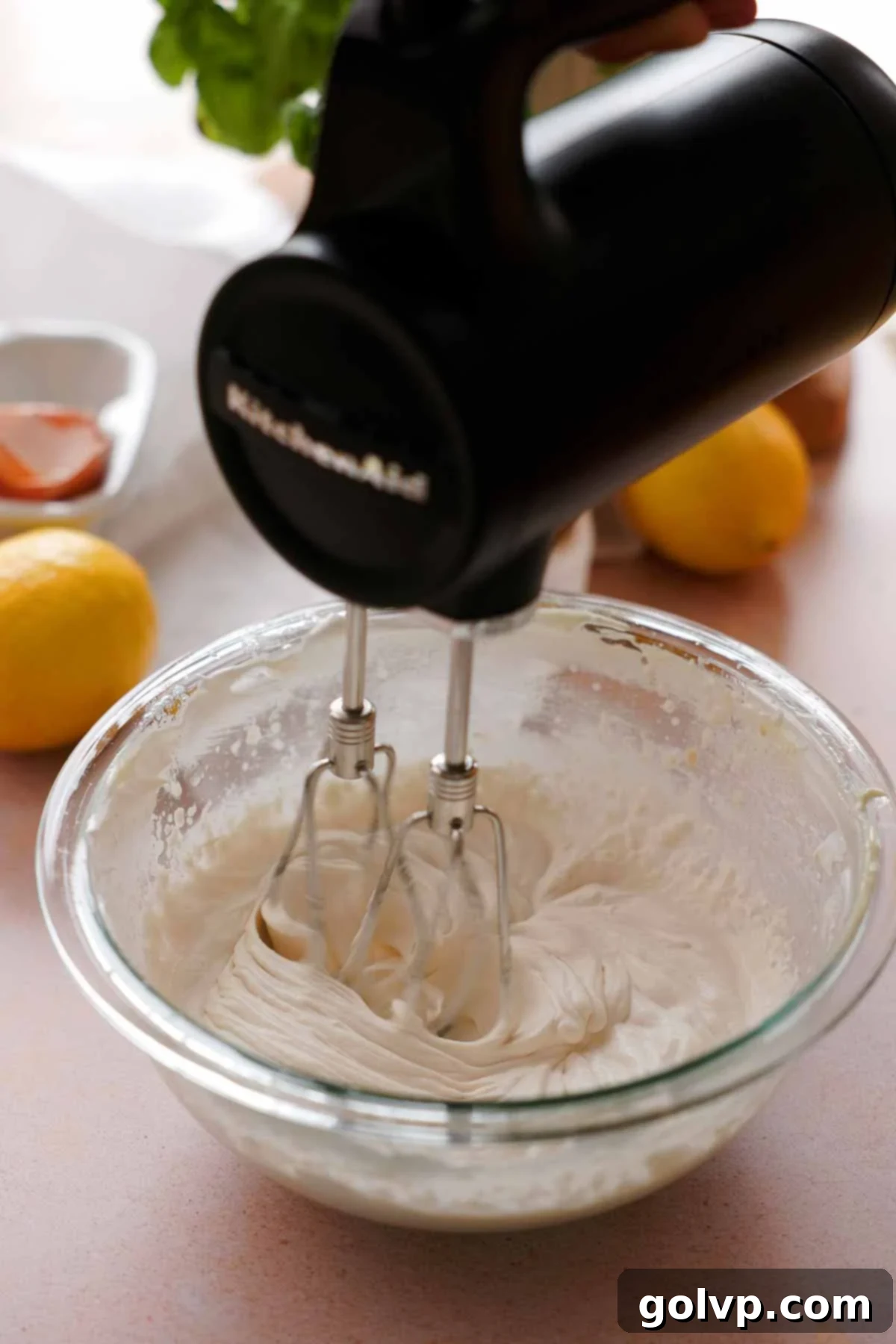 Whipping heavy cream to stiff peaks in a clean glass bowl using an electric hand mixer.