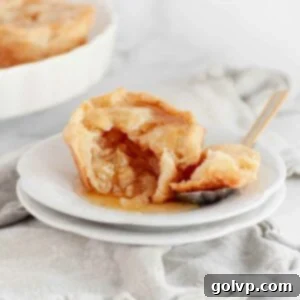 Mini apple pie on a white plate with a bite taken out, showing the apple filling.