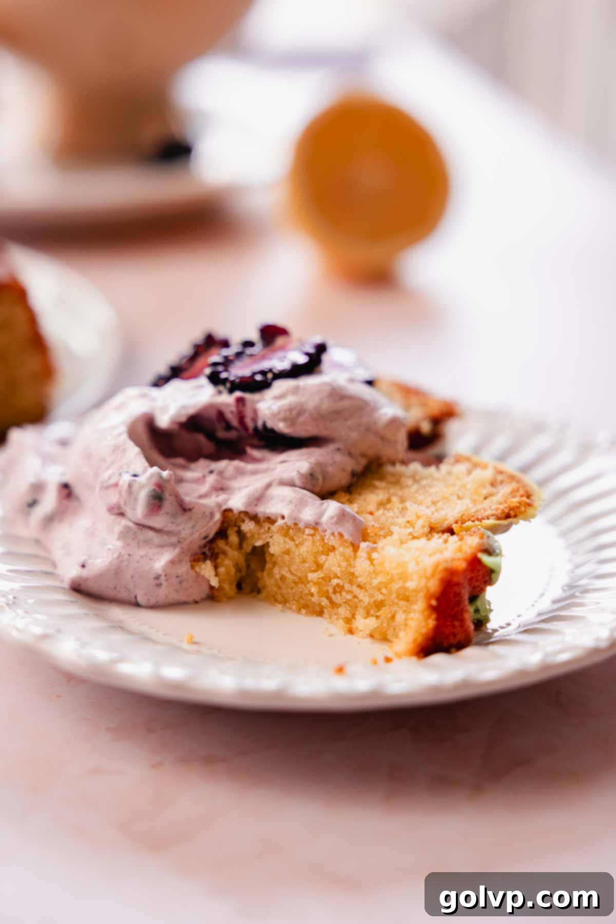 slice of lemon pound cake with a bite taken out, generously piled with blackberry whipped cream and fresh berries