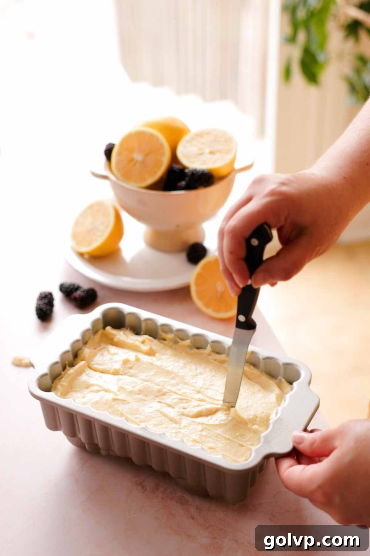 running a knife through the center of lemon pound cake batter in a prepared loaf pan before baking