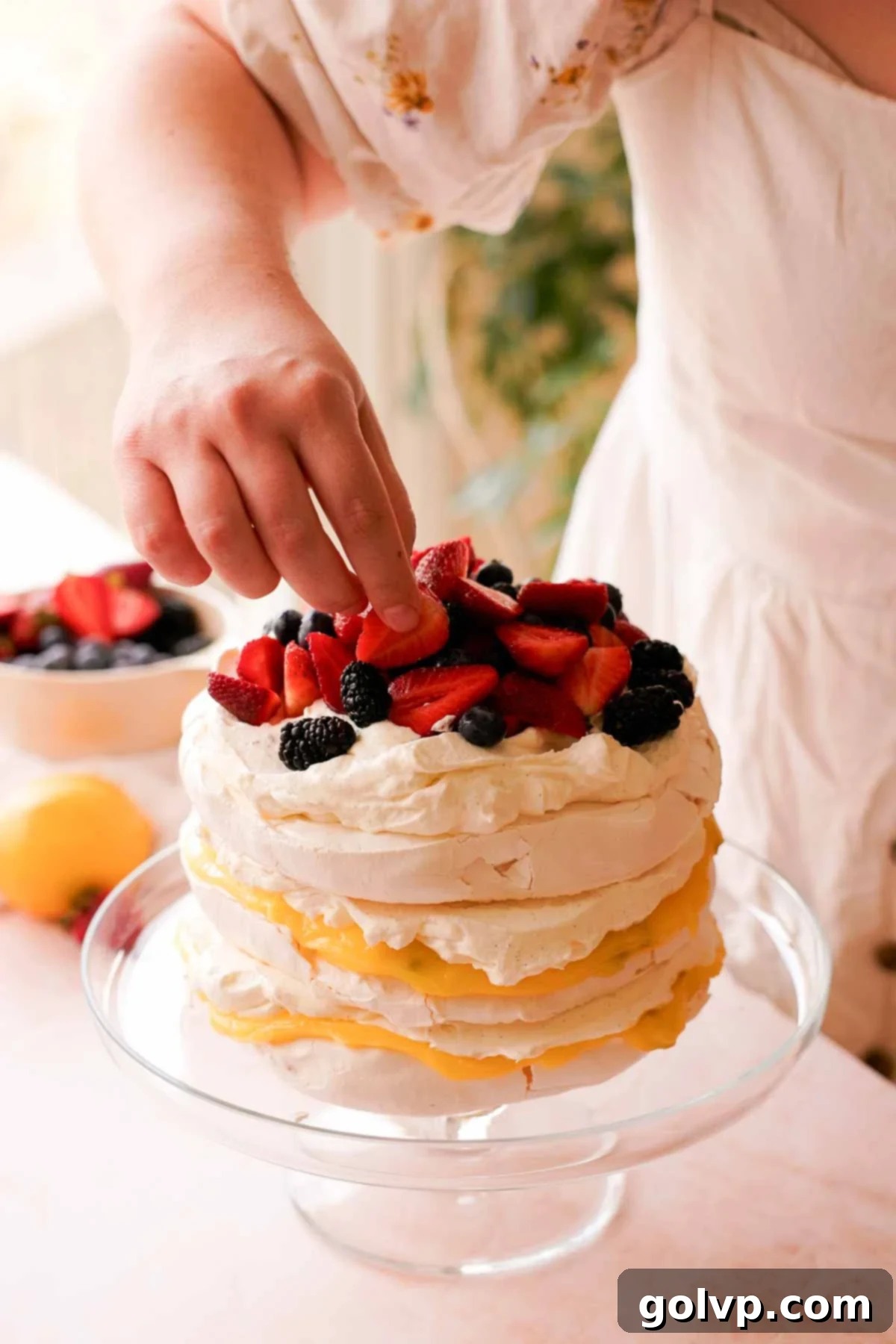 topping stacked pavlova cake with berries