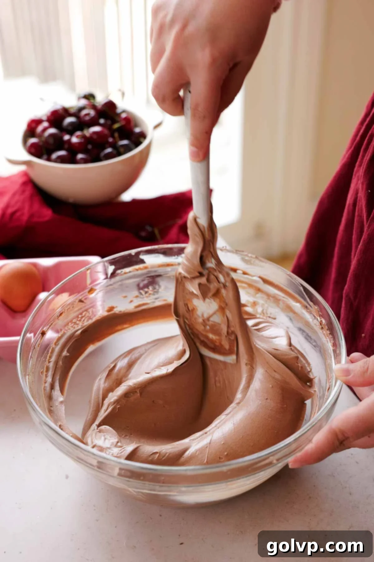 folding chocolate cheesecake batter with spatula in large glass bowl