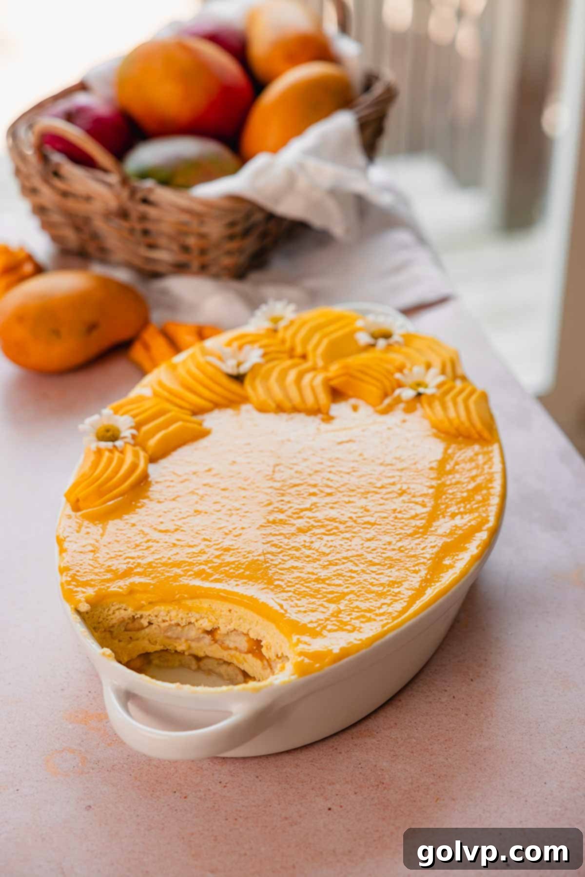 A beautifully presented mango tiramisu in a white ceramic baking dish, garnished with vibrant mango curd and fresh slices of ripe mango, ready to be served.