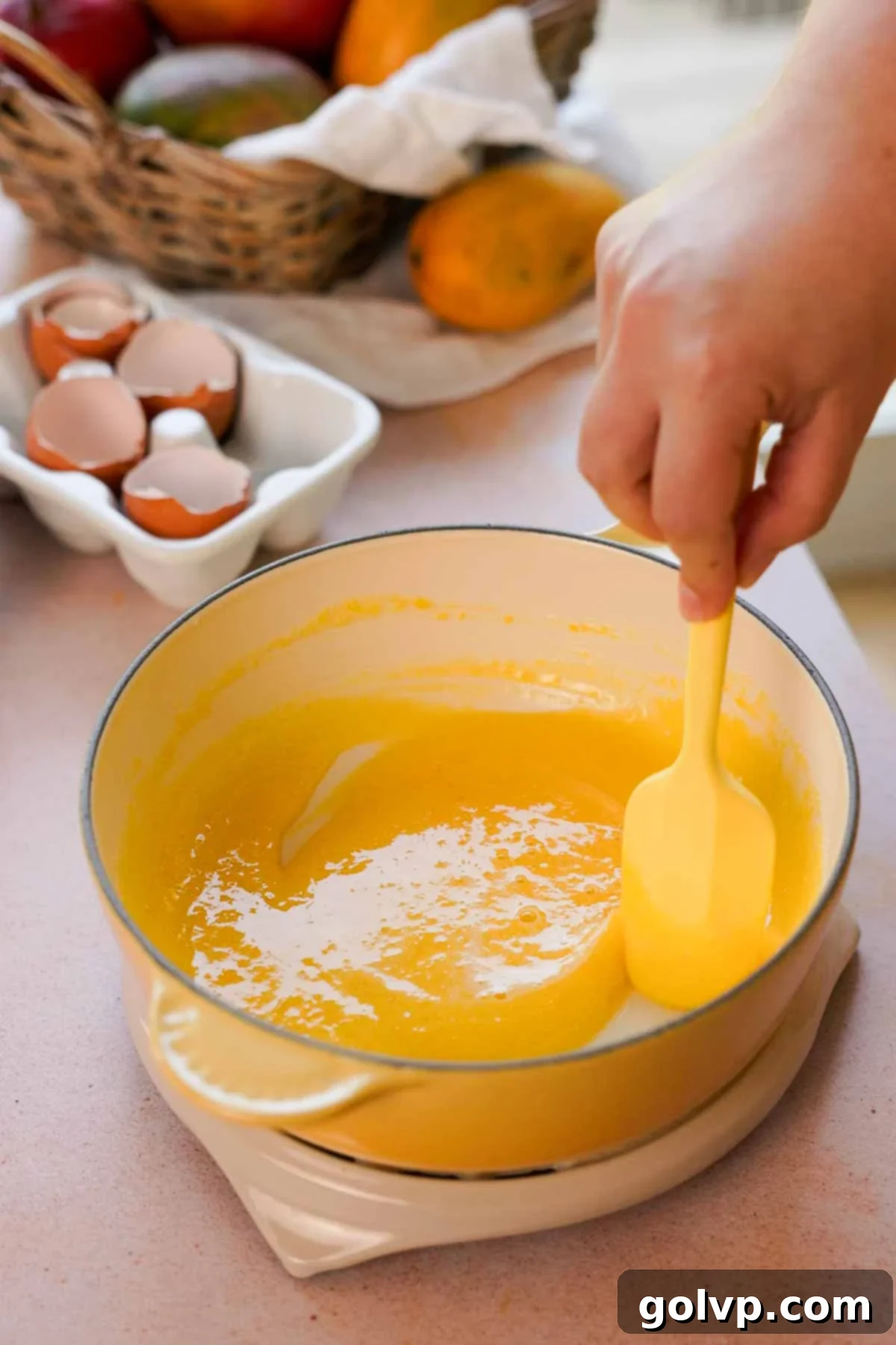 Egg yolks and granulated sugar being stirred together in a saucepan, forming a smooth, pale yellow mixture for the mango curd base.
