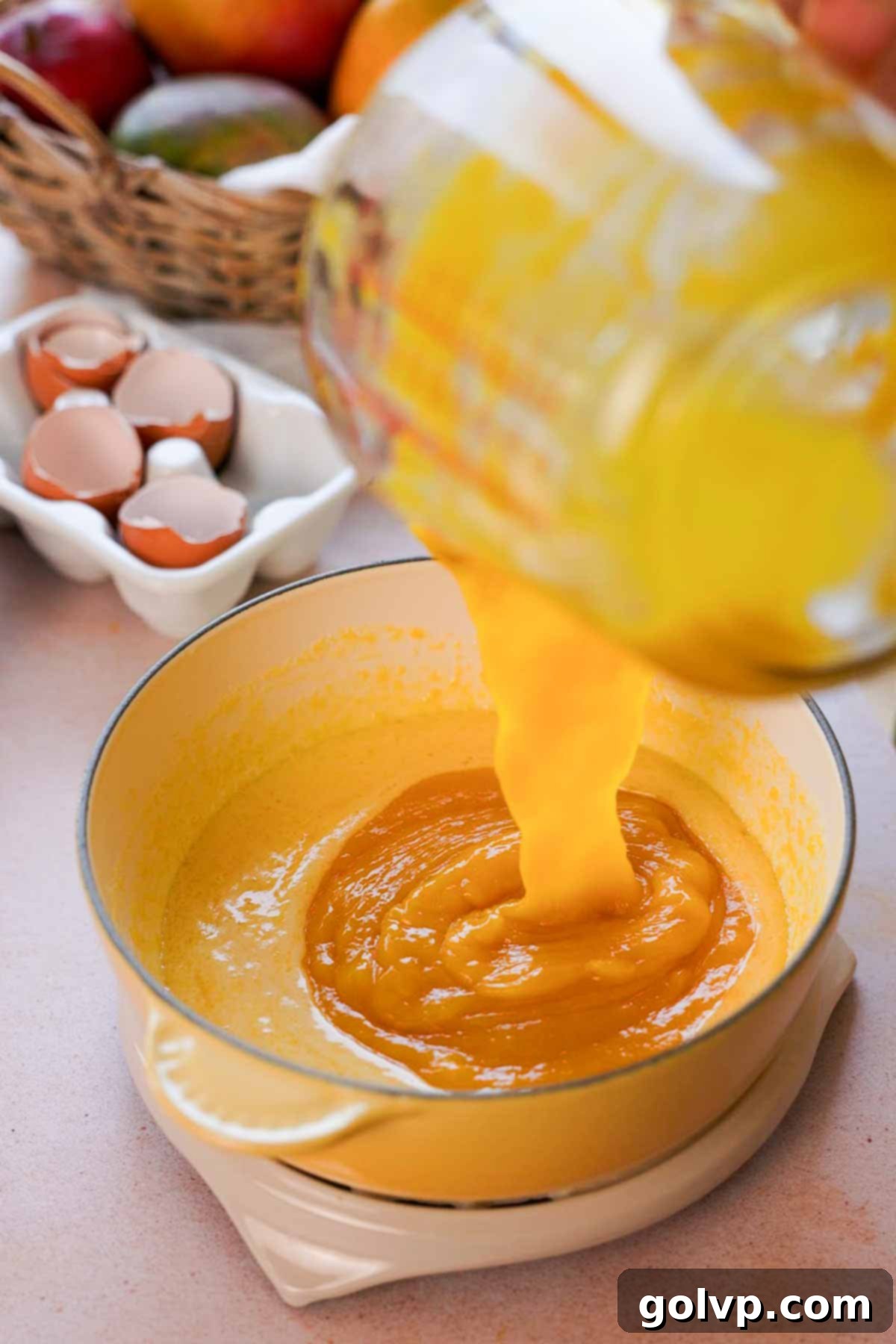 Mango puree being carefully poured into the saucepan with the egg yolk and sugar mixture, ready to be cooked into curd.