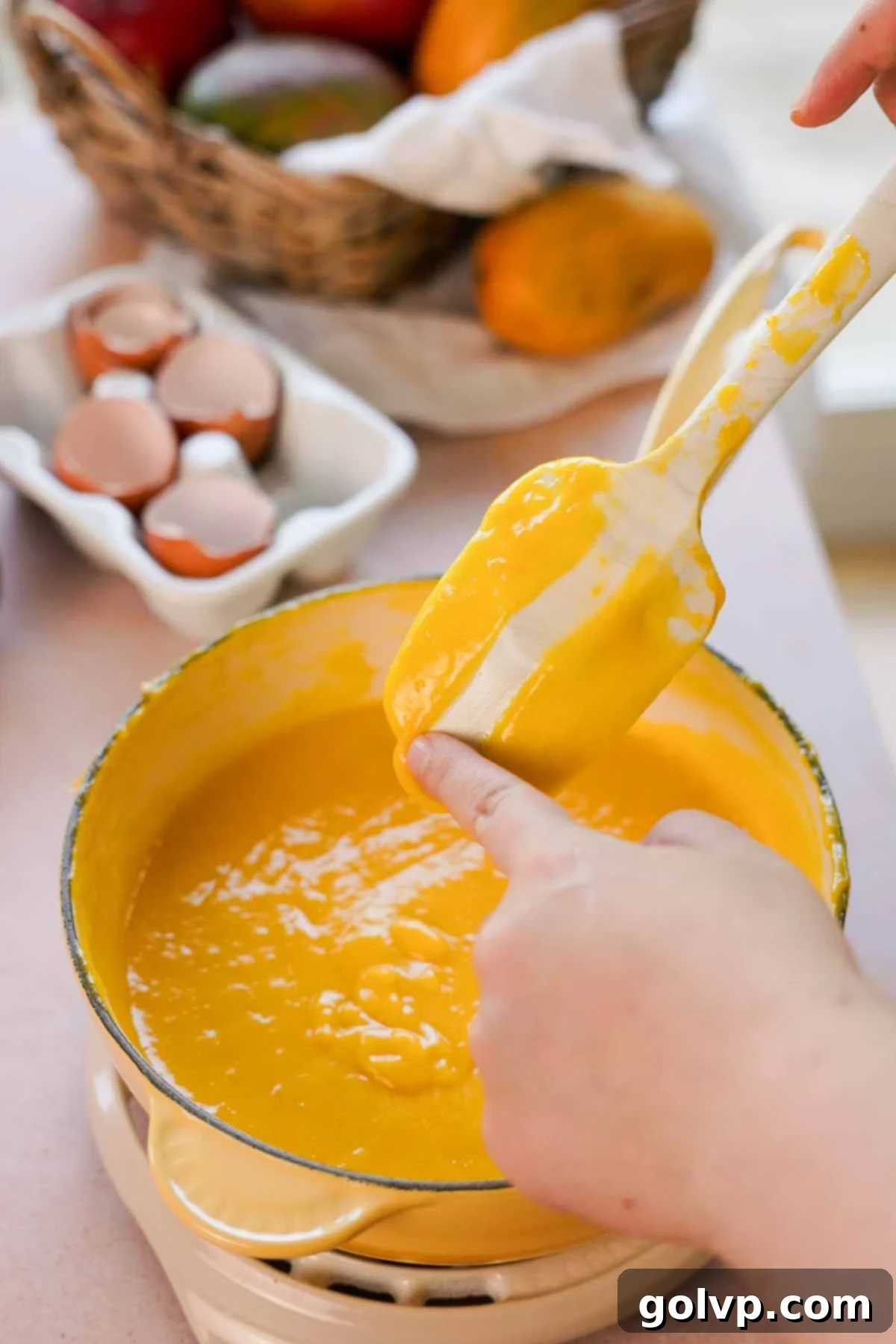 A spoon lifted from a saucepan, displaying the perfectly cooked and thickened mango curd clinging to its back, indicating proper consistency.