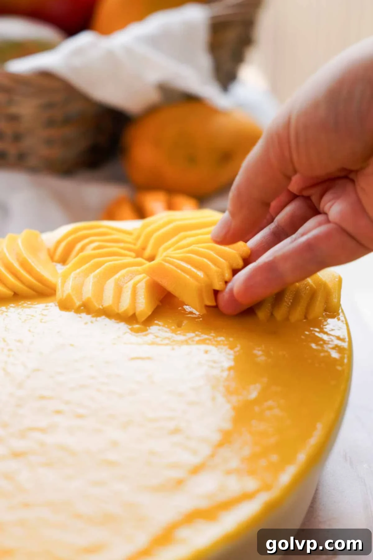 Thinly sliced fresh mangoes being artfully arranged on top of a finished mango tiramisu, ready for final touches and serving.