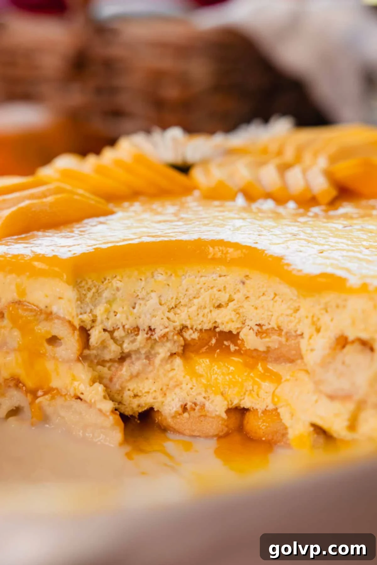 A close-up shot revealing the creamy, layered texture of mango tiramisu in a white dish, garnished with mango pieces, highlighting its luxurious consistency.