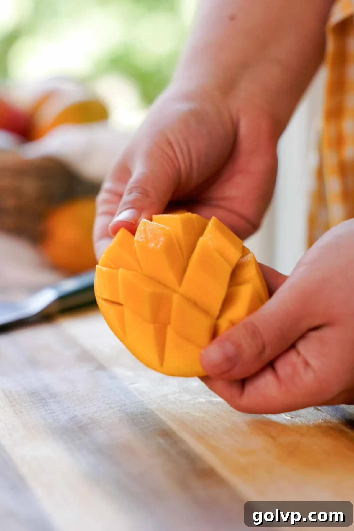 A hand demonstrating how to flip a mango skin inside out to easily release the cubed mango chunks after scoring the flesh.