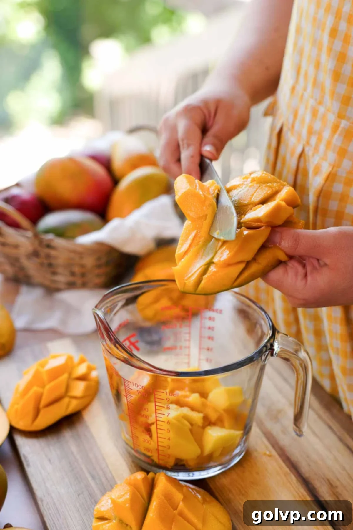 A sharp knife slicing cubed mango flesh directly off the skin into a measuring cup for accurate portioning.