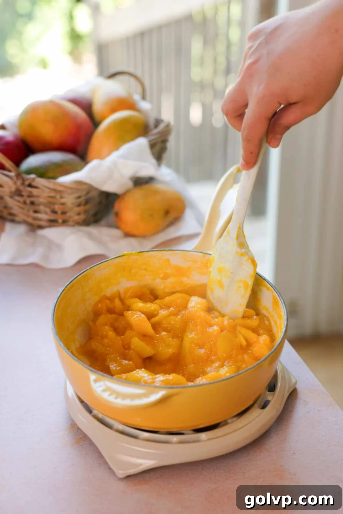 Mango chunks simmering in a saucepan with sugar and water, visibly thickening as they cook down.