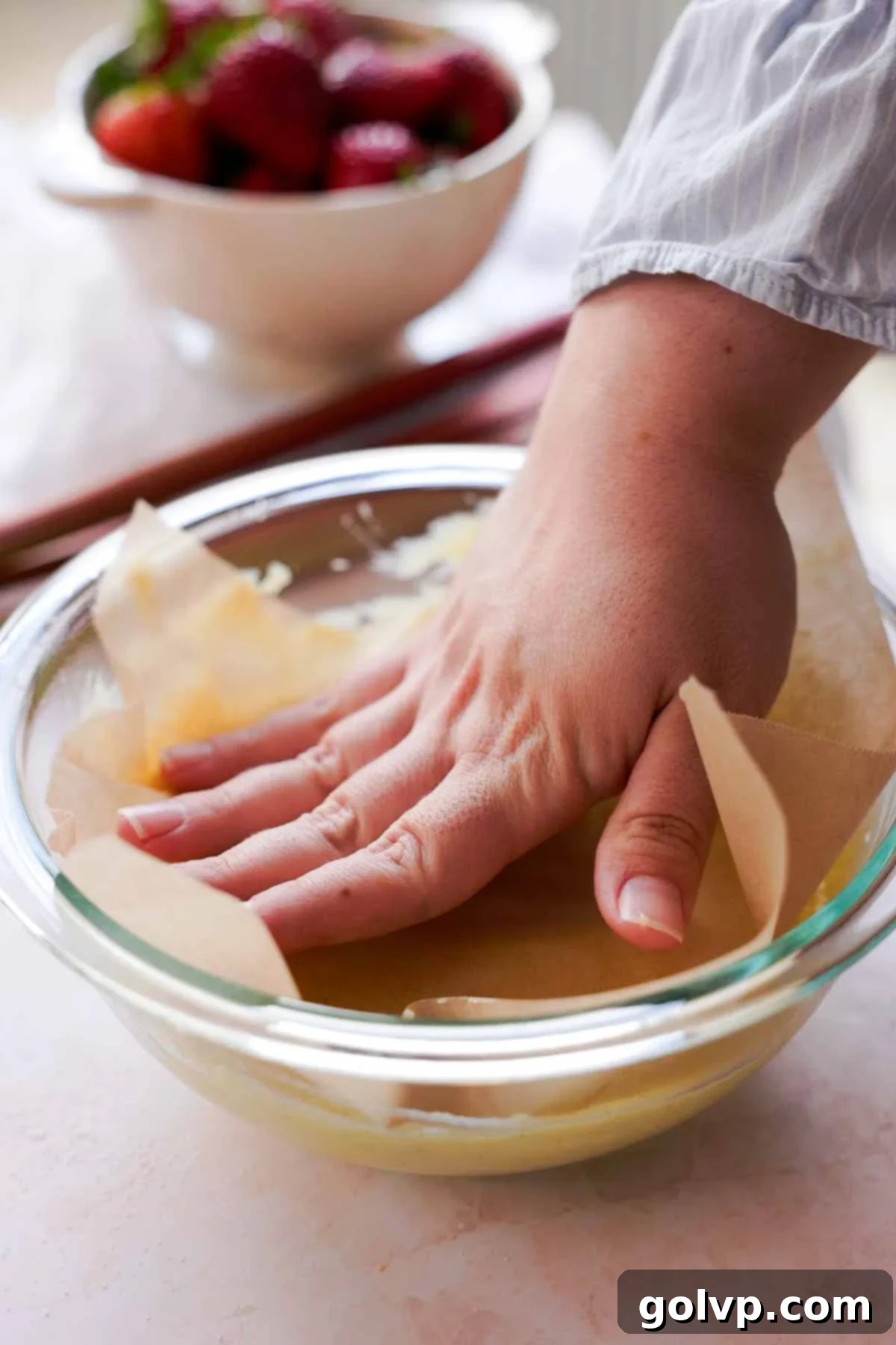 pressing down parchment paper onto bowl of hot custard