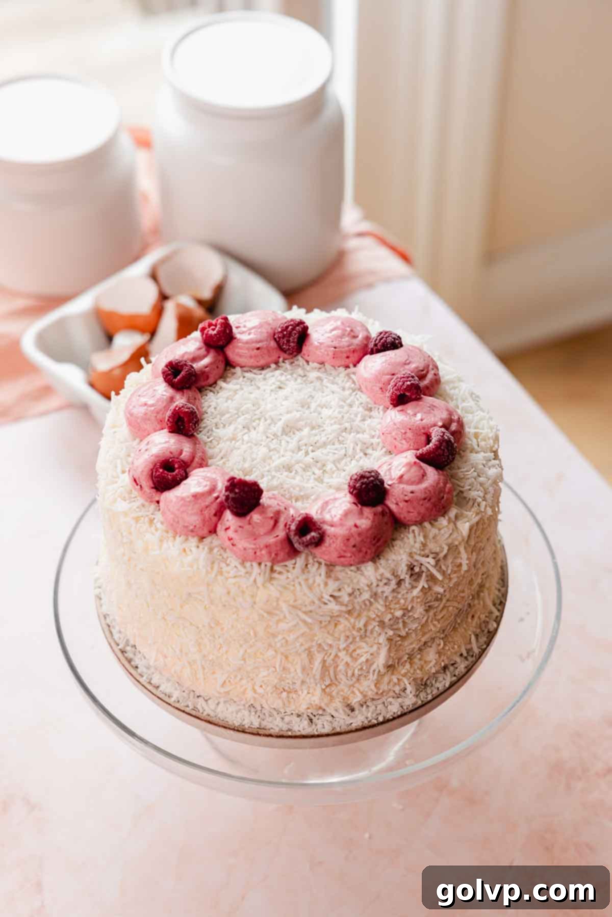 coconut cake covered in coconut shavings decorated with raspberries