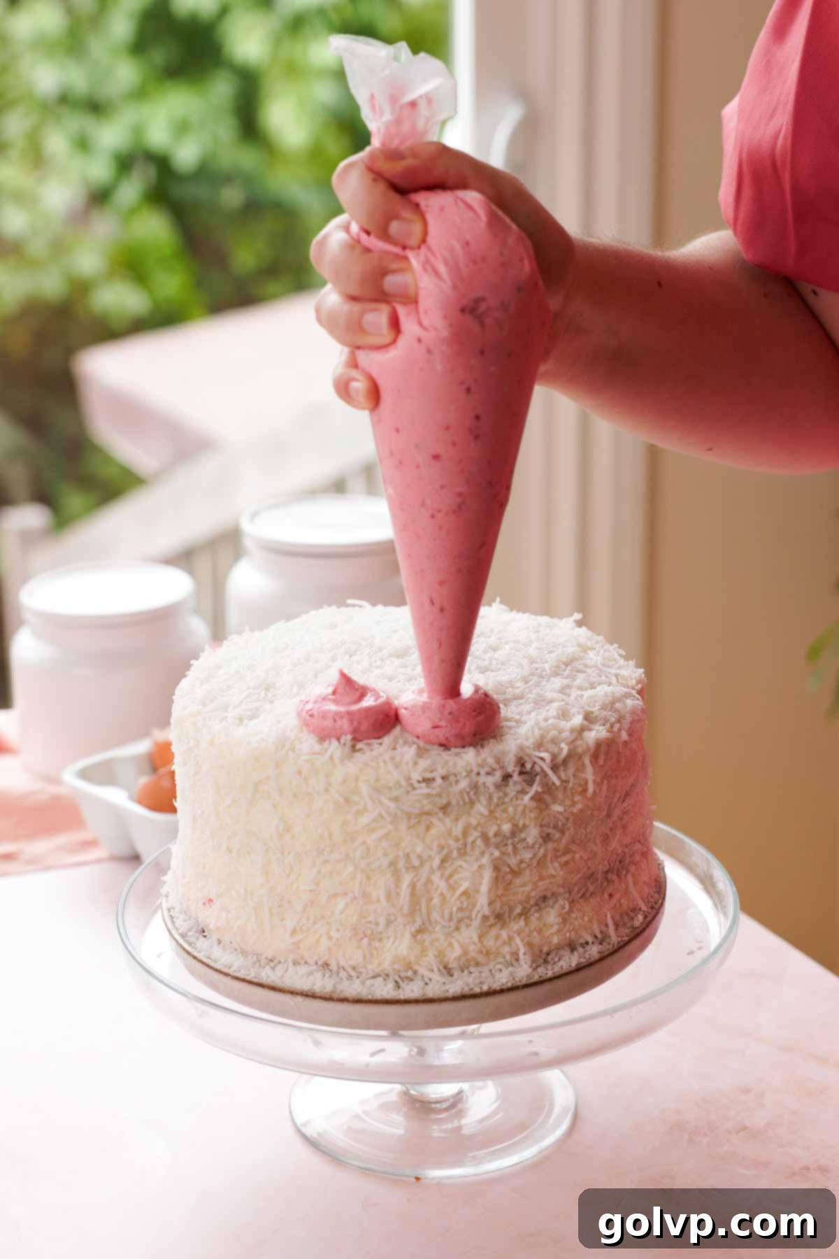piping dollops of raspberry frosting onto the coconut raspberry cake