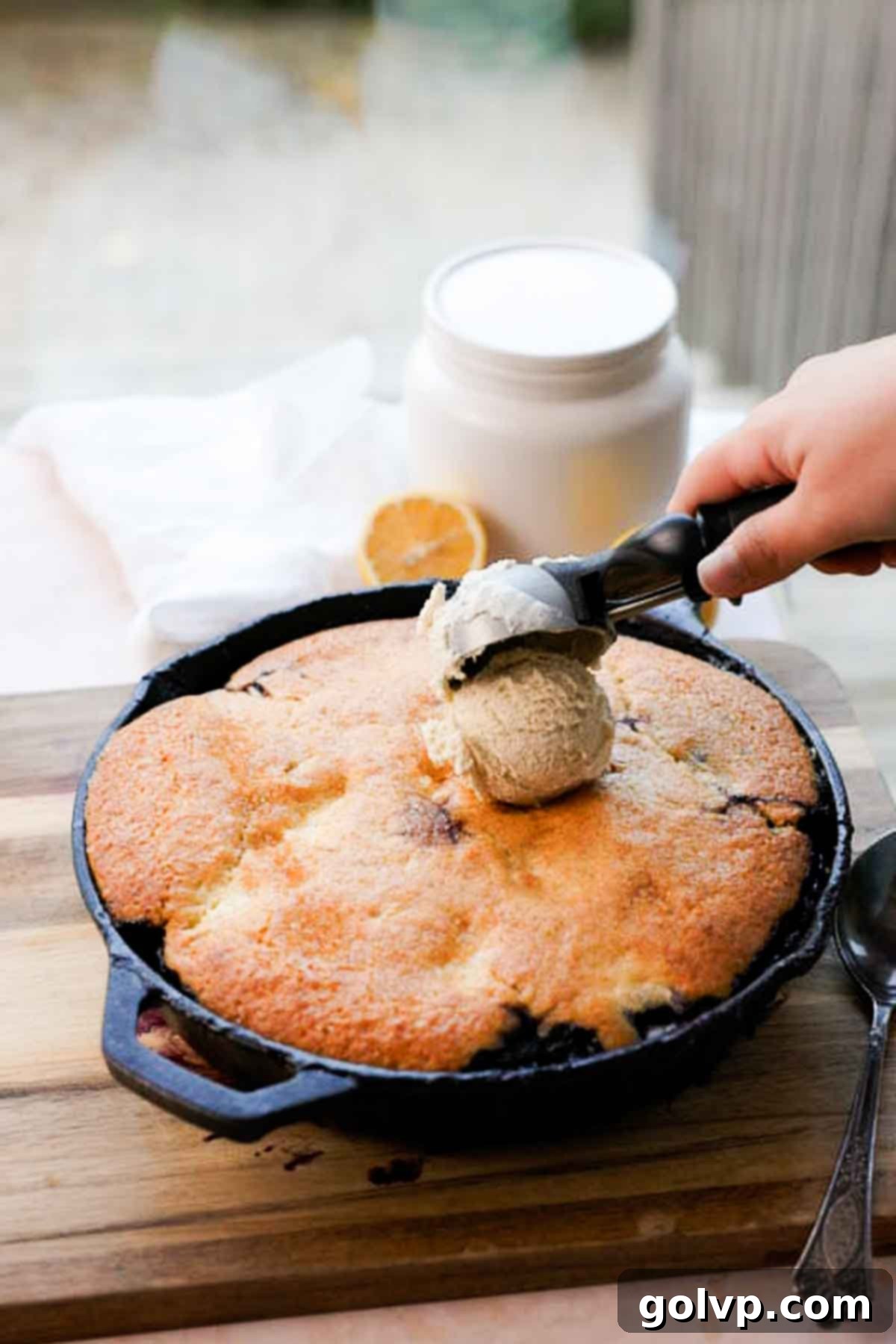 scooping vanilla ice cream onto blueberry lemon cream cheese cobbler