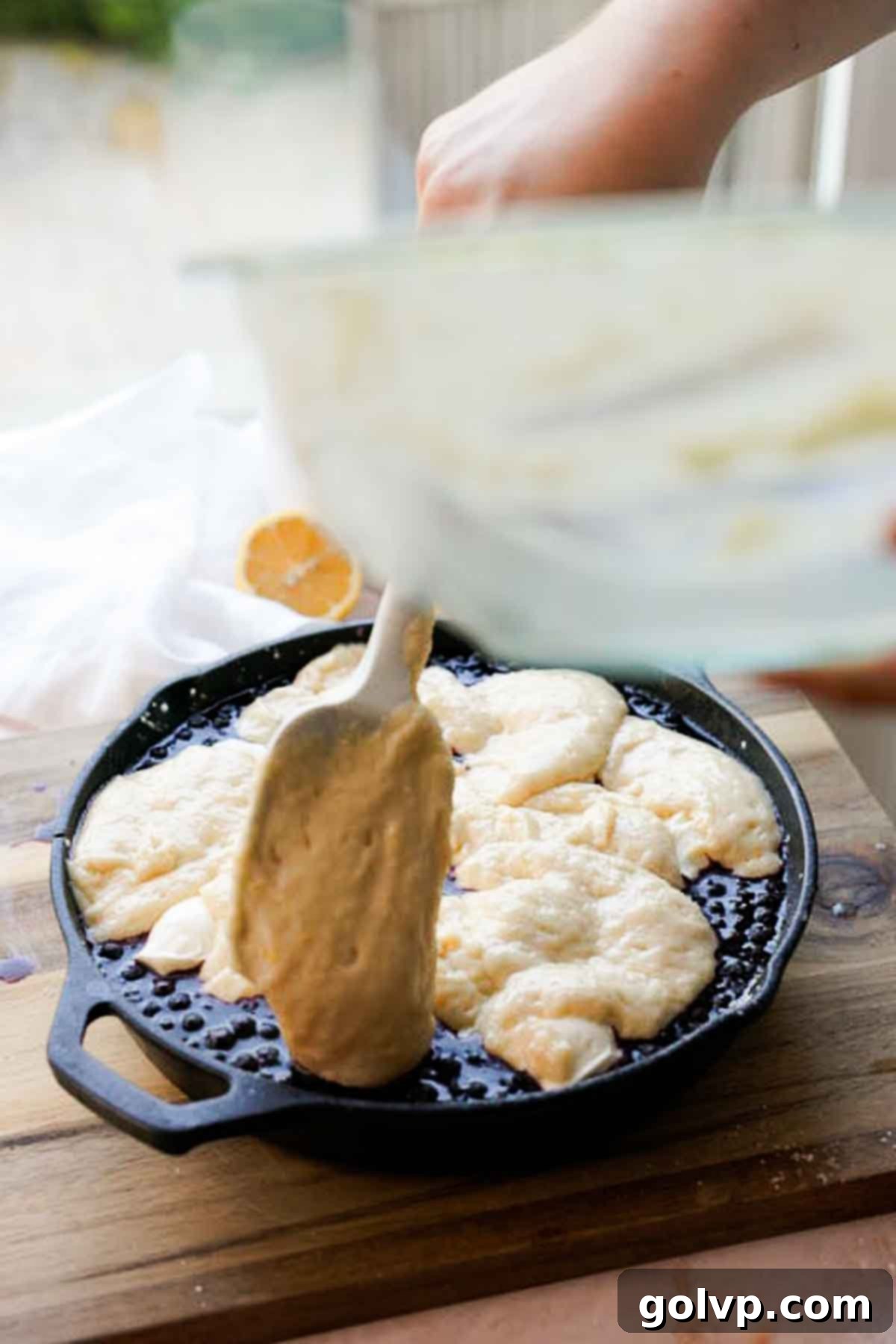 adding lemon cobbler batter onto blueberry cobbler